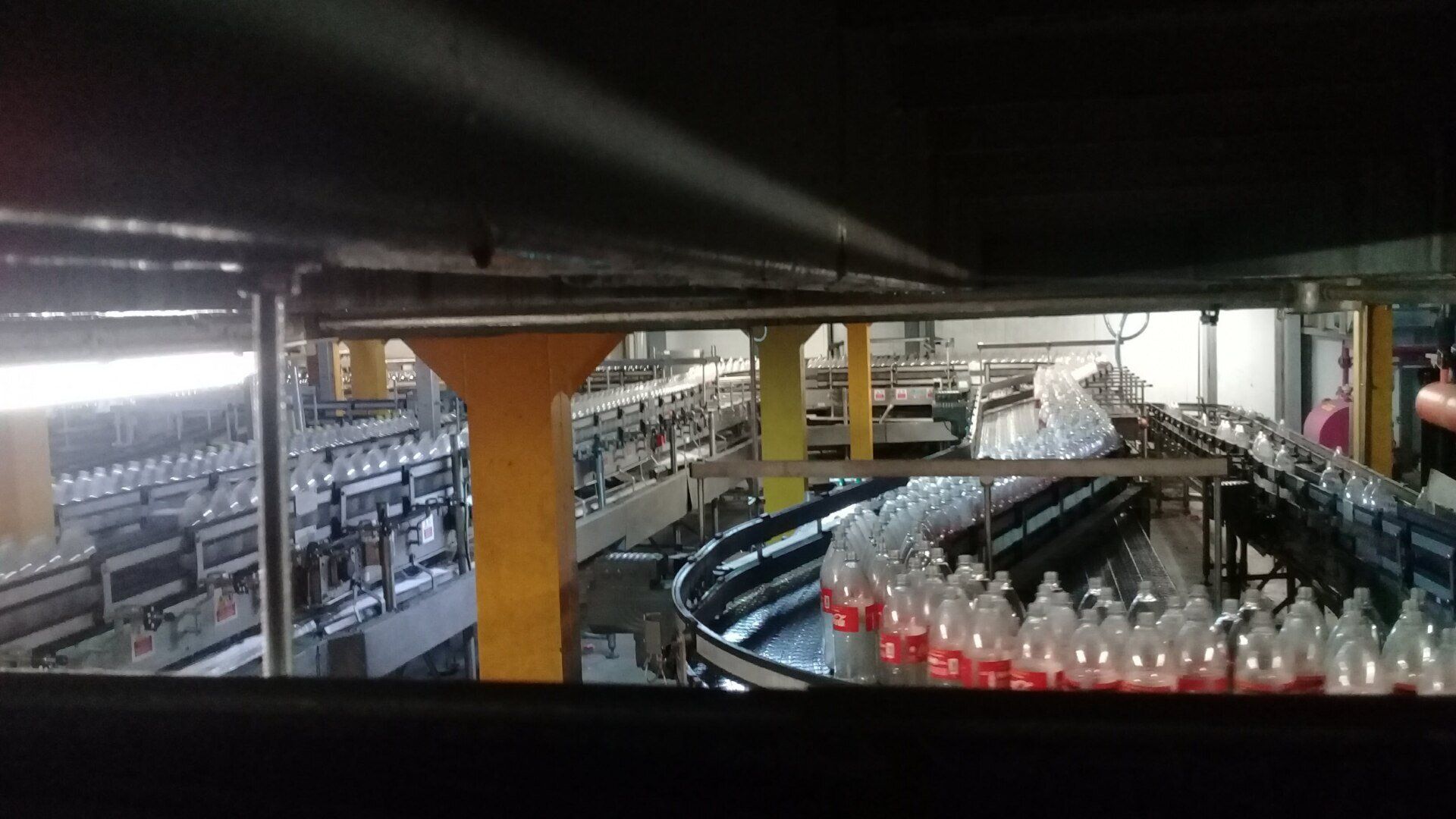 Botellas de plástico en una cinta transportadora en una planta embotelladora industrial muy iluminada.