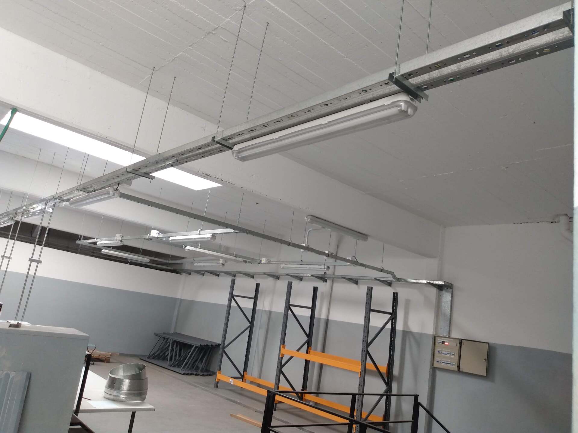 Una habitación con estilo de almacén, con lámparas colgantes, estanterías metálicas y paredes grises.