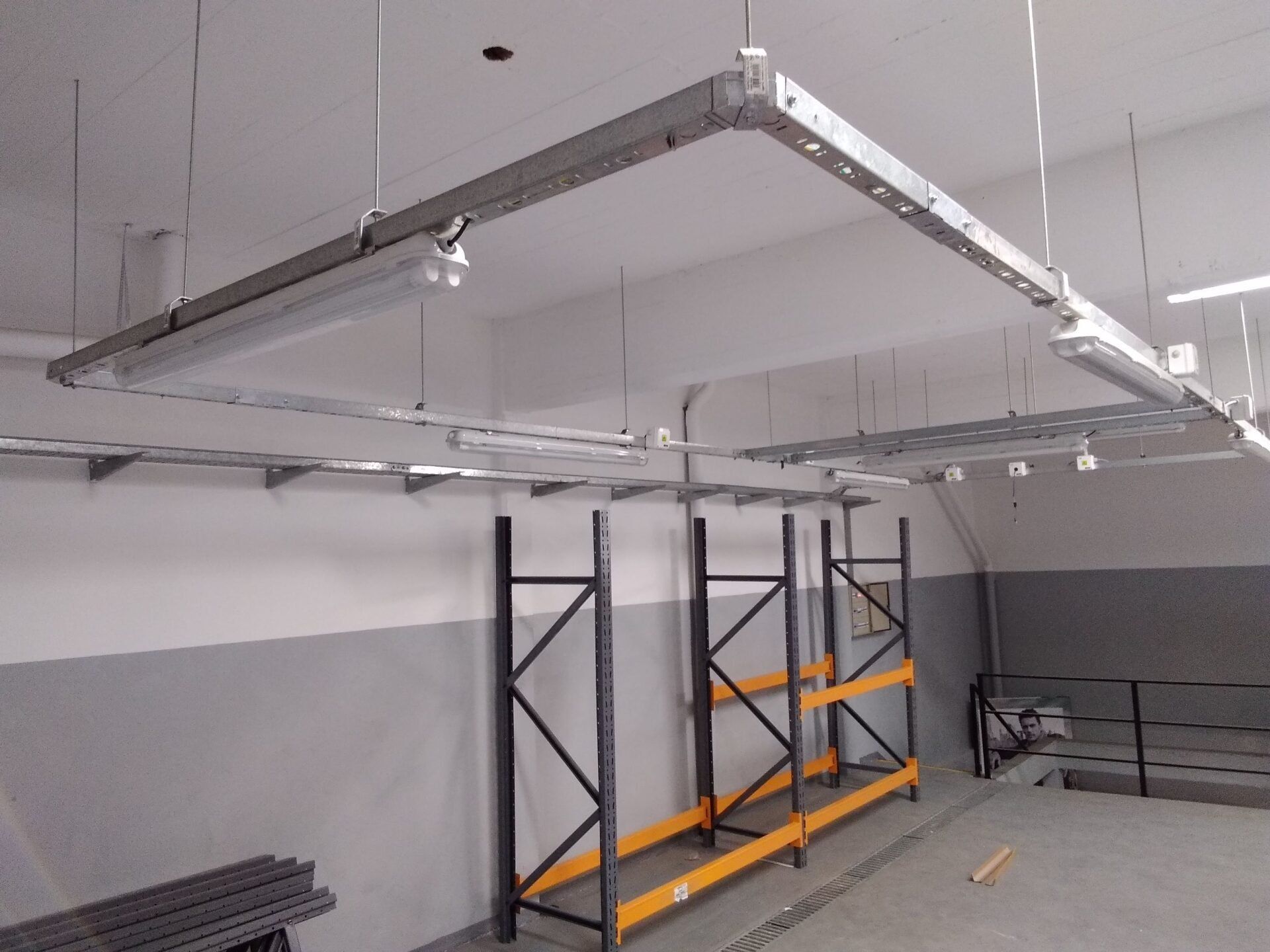 Una estructura metálica suspendida de un techo blanco sobre estanterías de almacén en una habitación