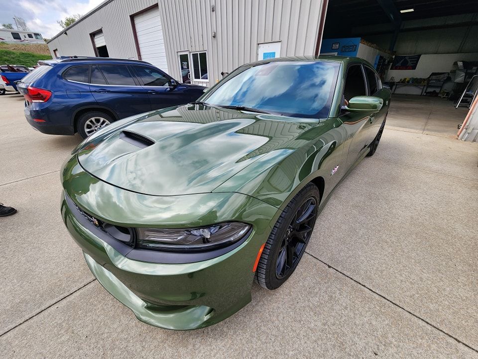 A green dodge charger is parked in a parking lot in front of a building.