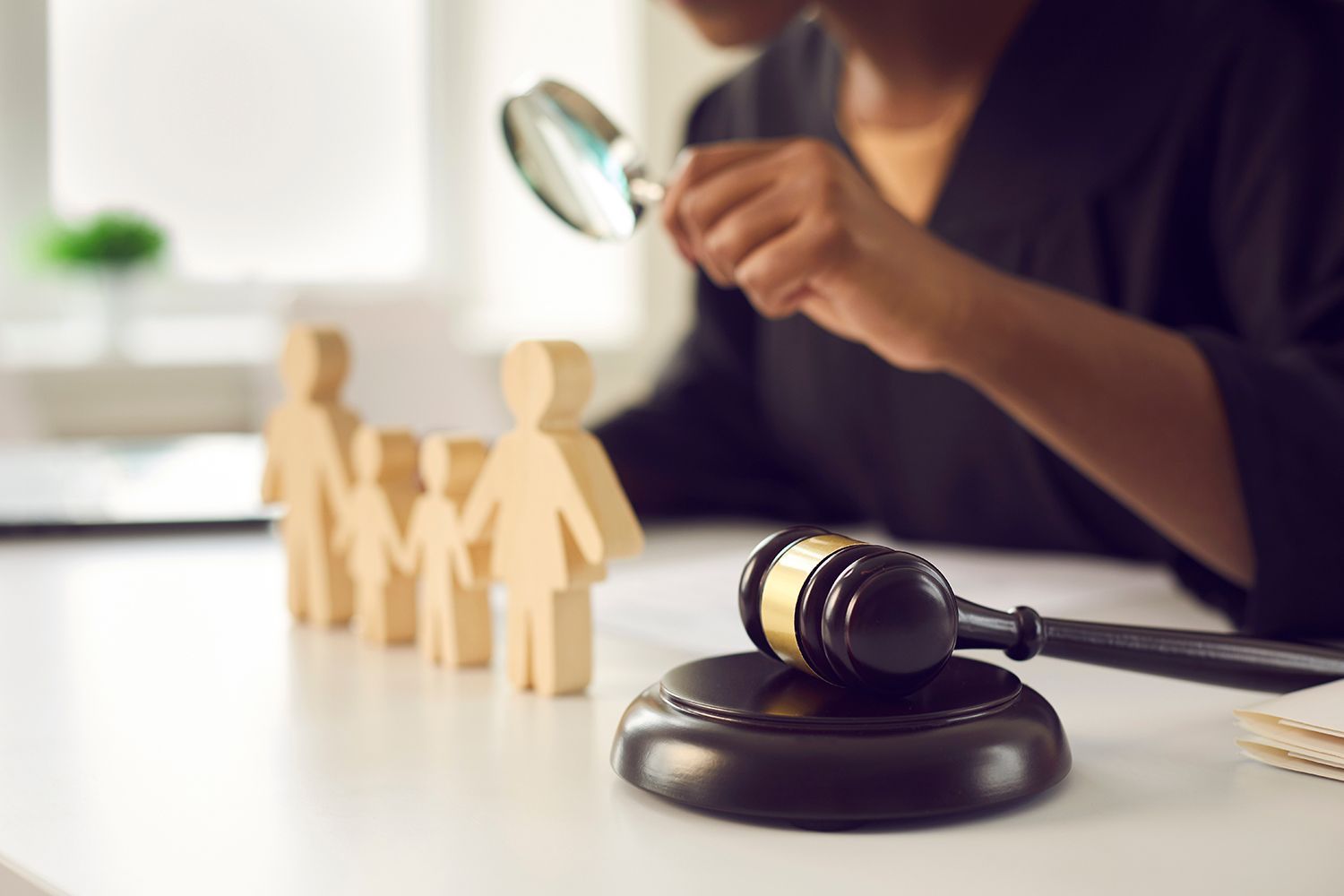 A courtroom gavel beside wooden family figures as legal documents are reviewed at a desk.