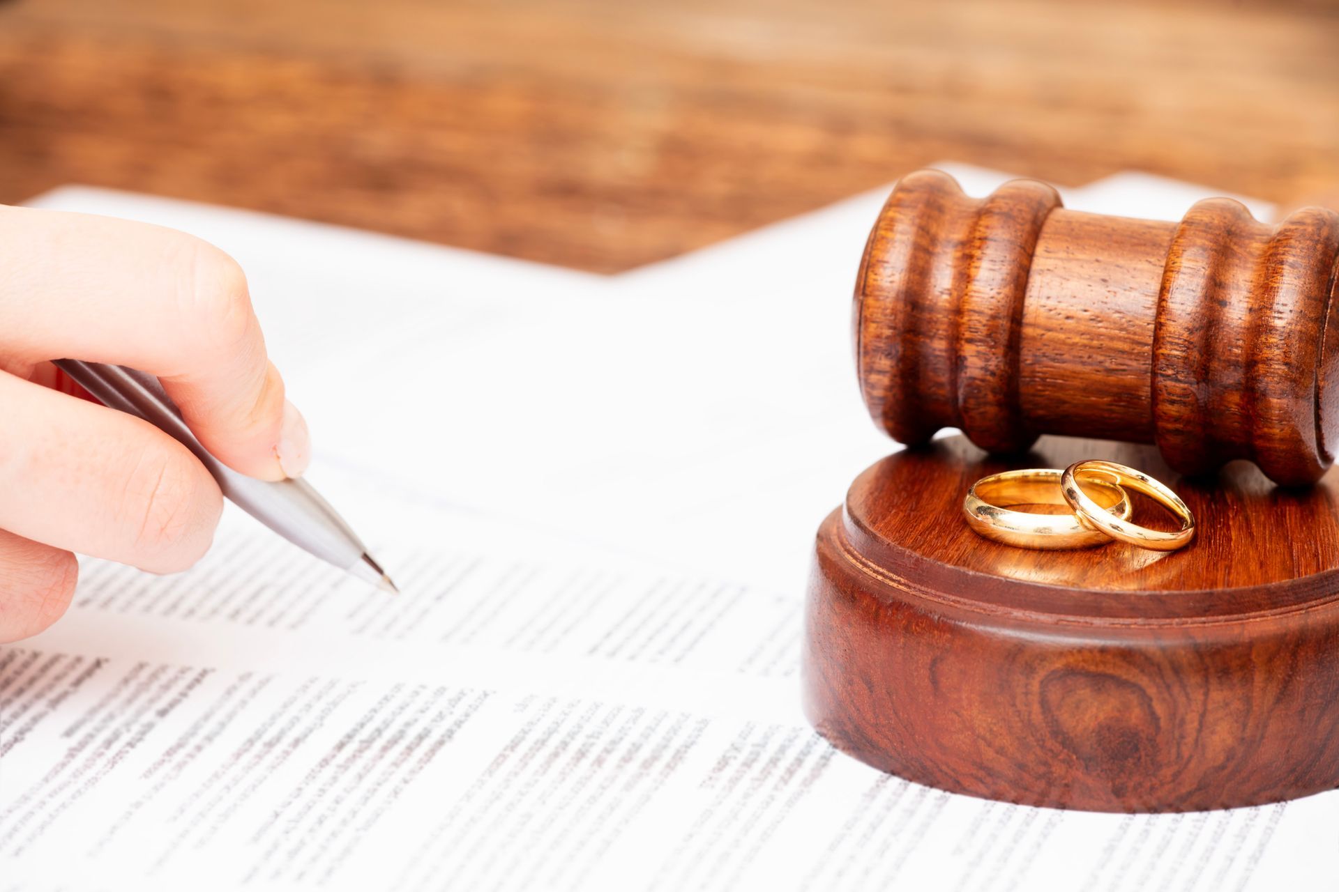 Divorce lawyer document being signed next to gavel and wedding rings symbolizing separation.