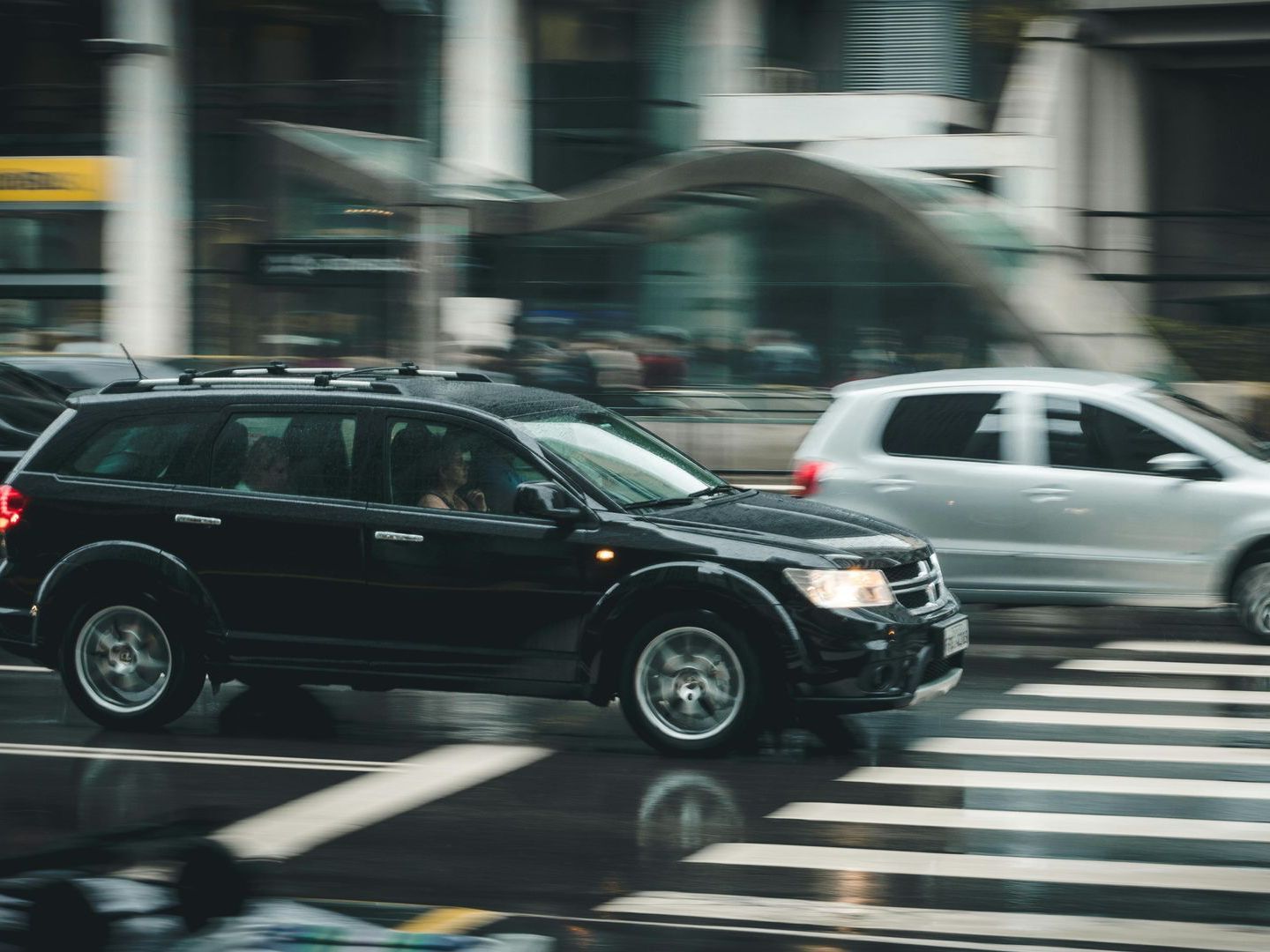 A black suv is driving down a city street in the rain.