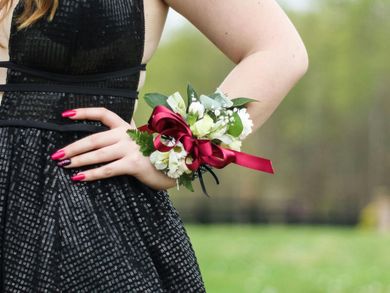 A woman in a black dress has a bouquet of flowers on her wrist