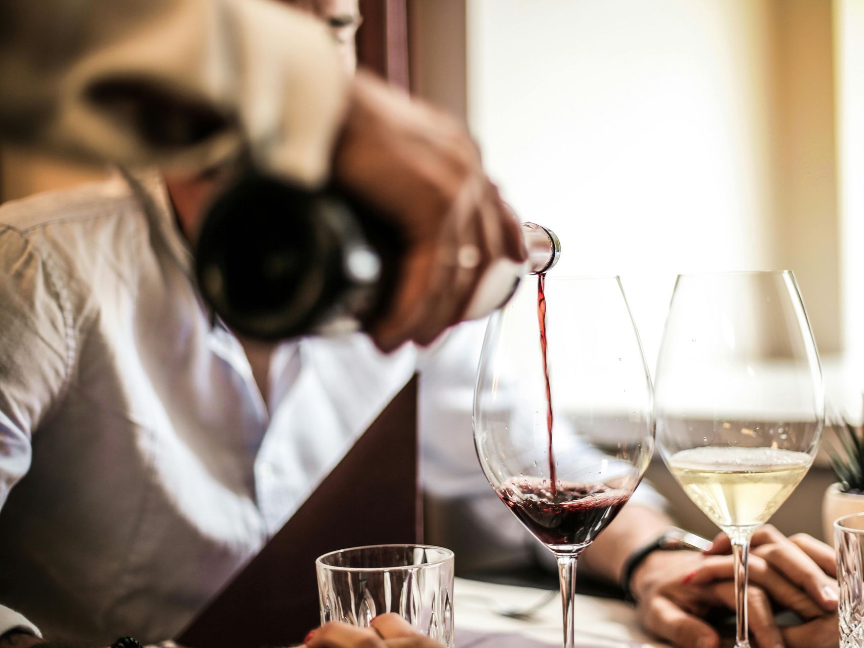 A man is pouring wine into a glass at a table.