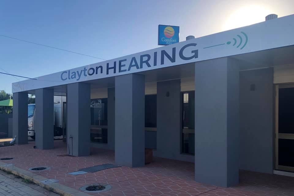 A Pair of Hearing Aids Are Sitting on a Wooden Table Next to a Case — Clayton Hearing in Pialba, QLD
