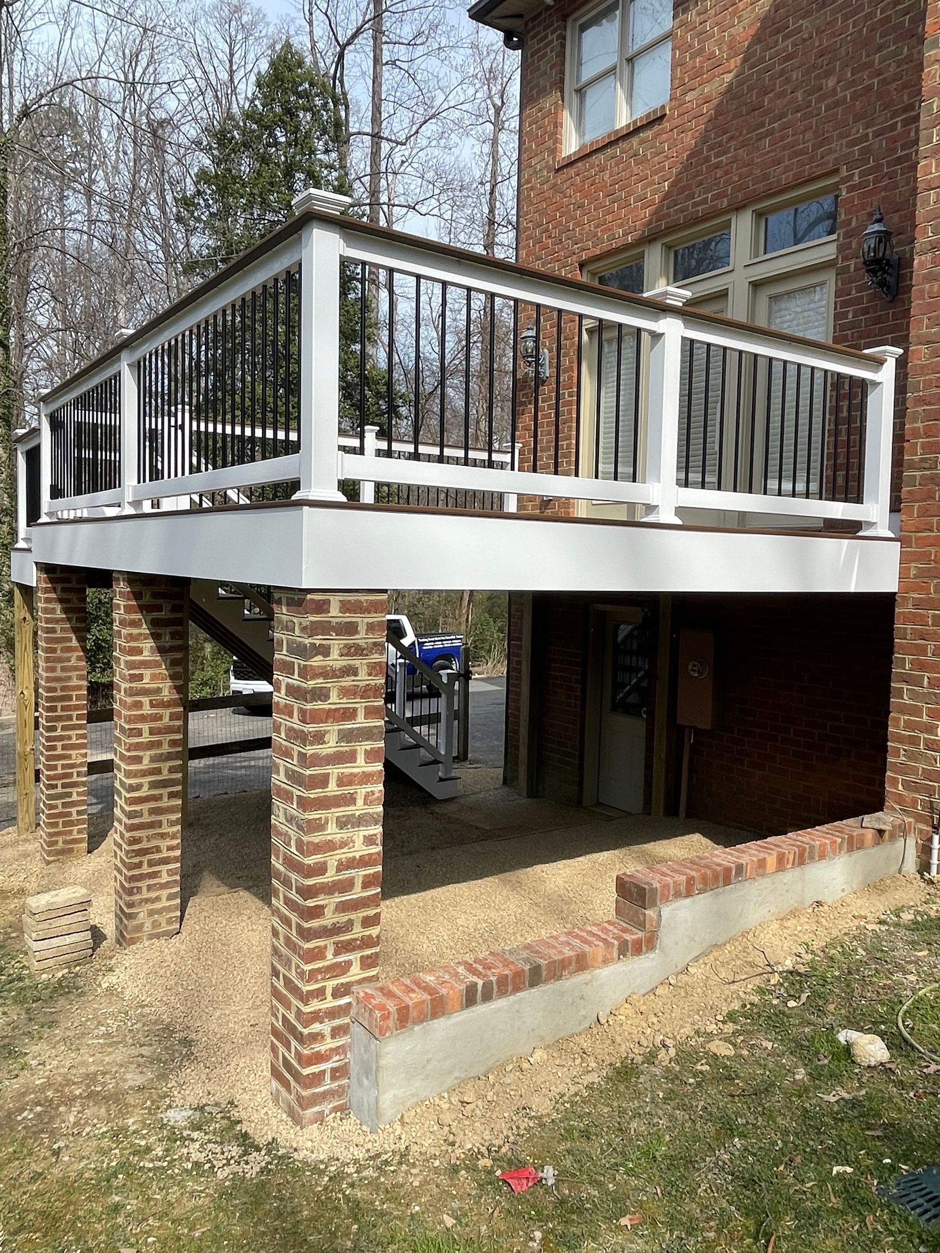A white deck with a black railing is under a brick house.