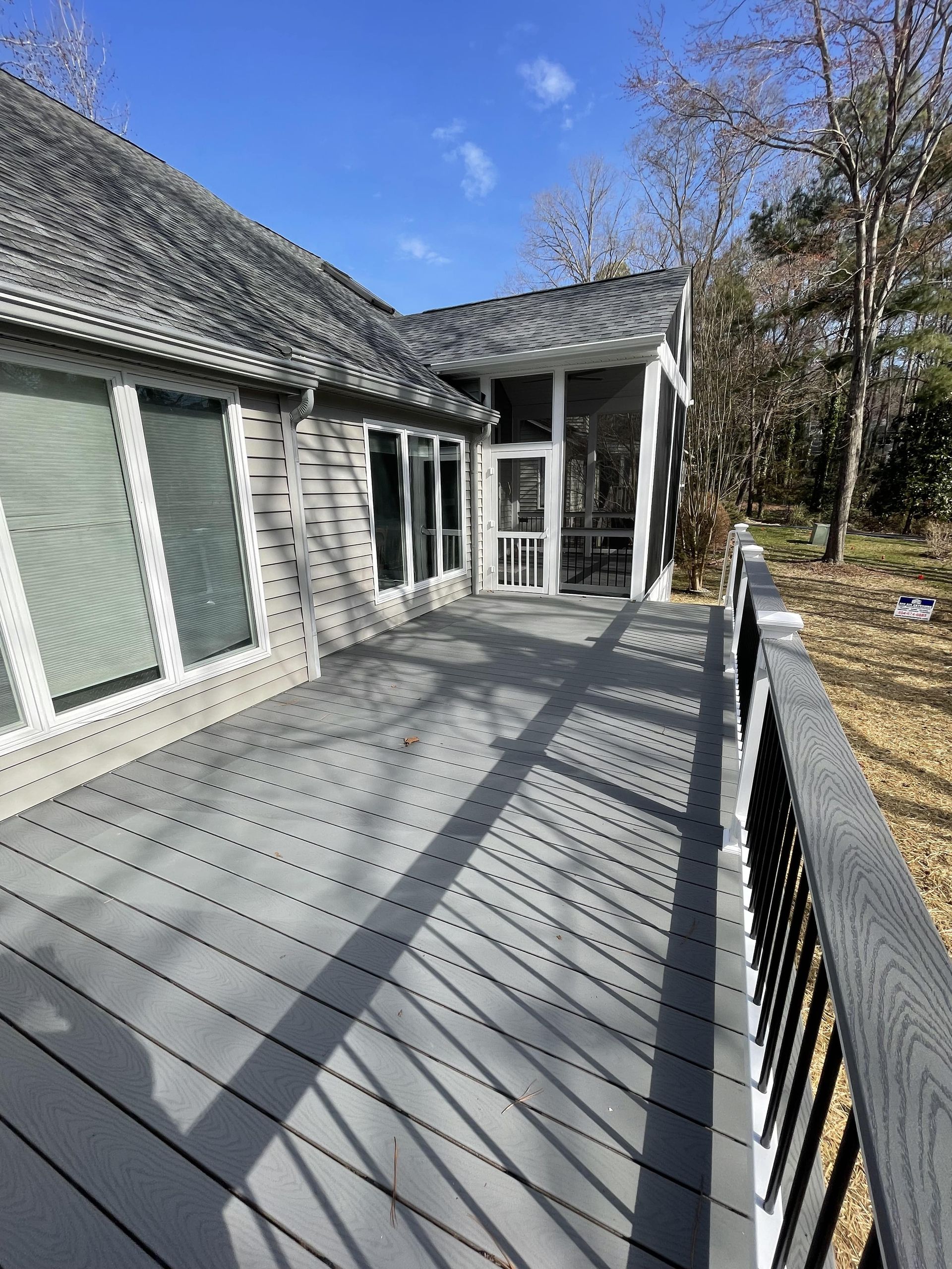 There is a large deck in front of a house with a screened in porch.