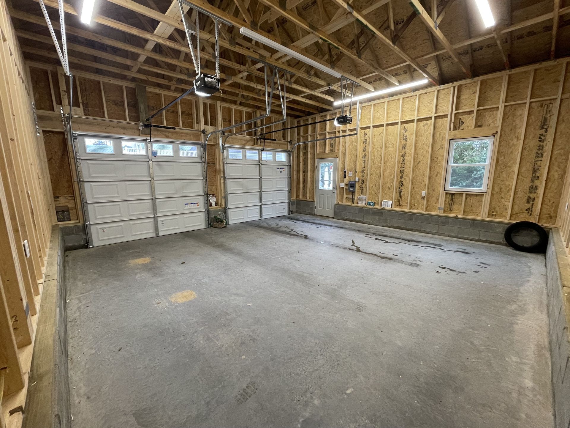 An empty garage with two garage doors and a tire on the floor.