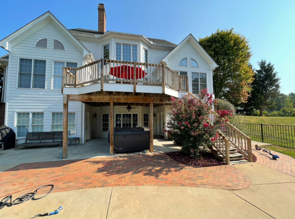Back of a white house with a two-story deck, red umbrella, hot tub, and brick patio.
