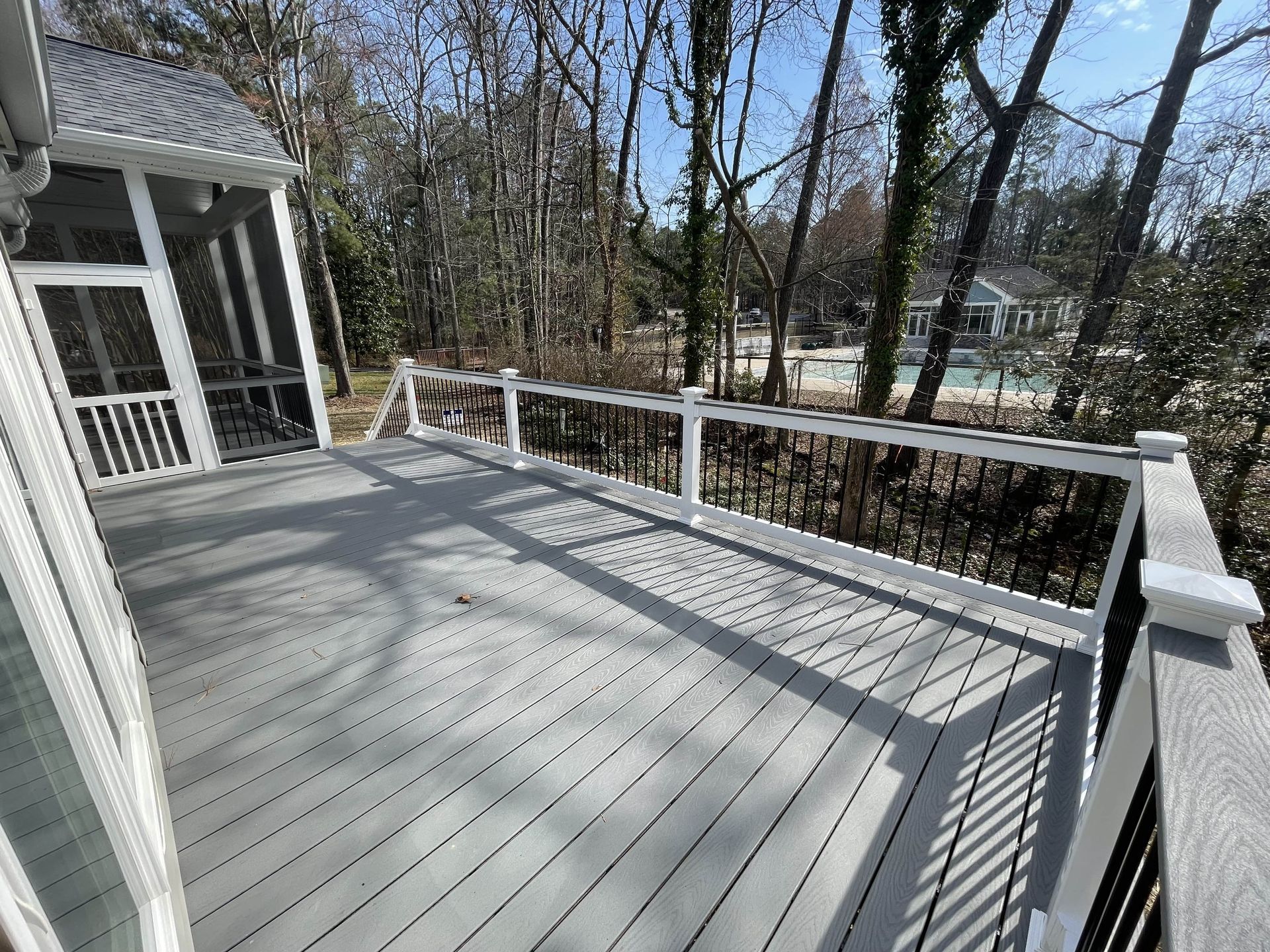 A large deck with a screened in porch and trees in the background.
