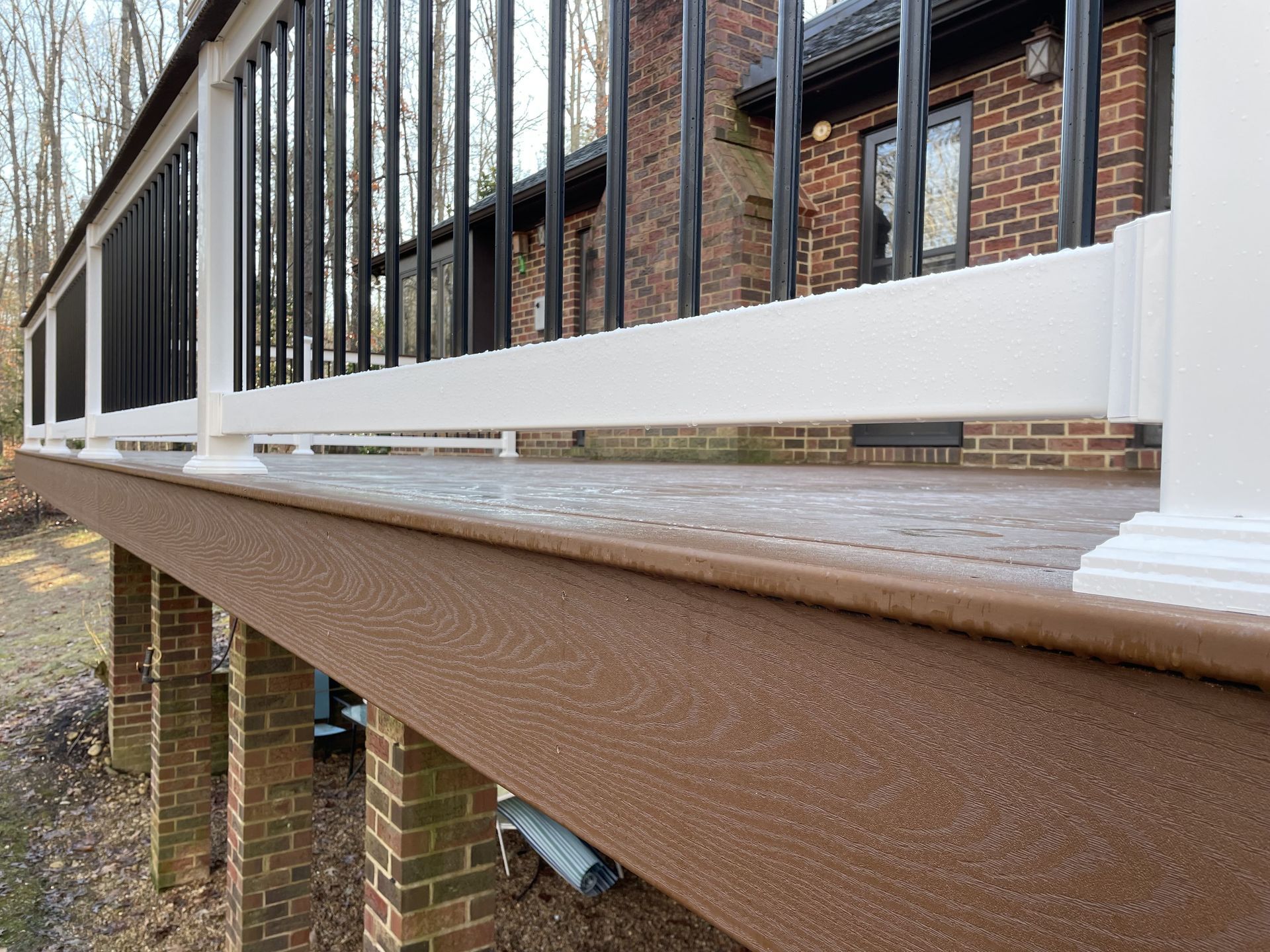 A deck with a white railing and a brick house in the background.