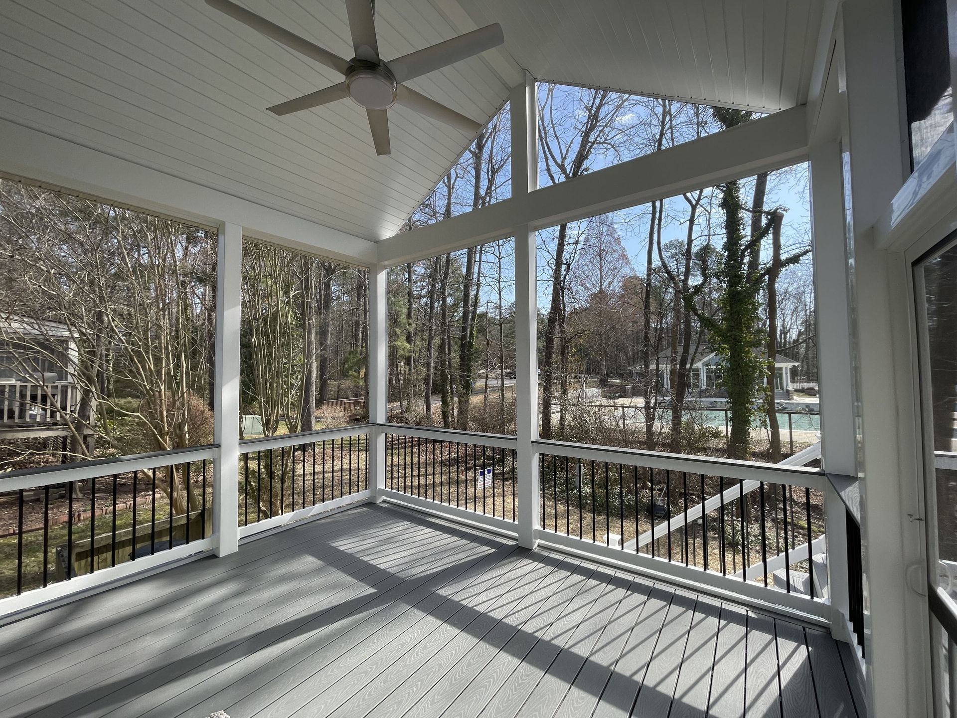 A screened in porch with a ceiling fan and trees in the background
