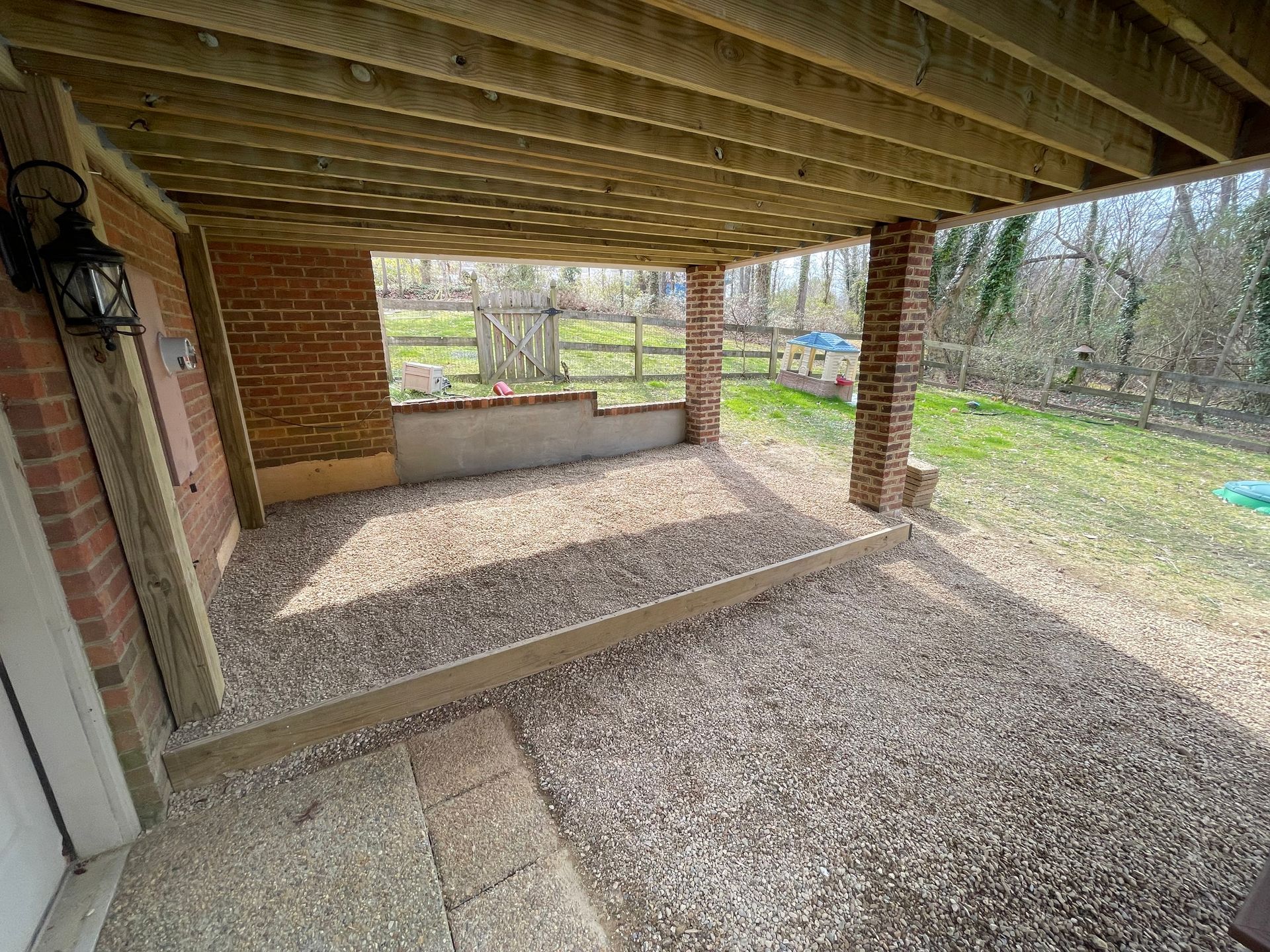 A covered patio with a wooden deck and gravel in front of a brick house.