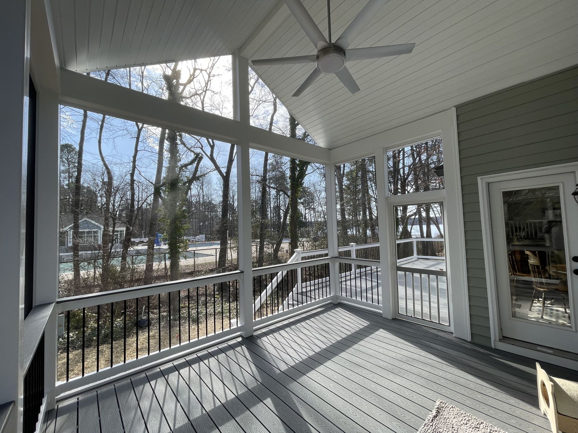 A screened in porch with a ceiling fan and a view of trees.