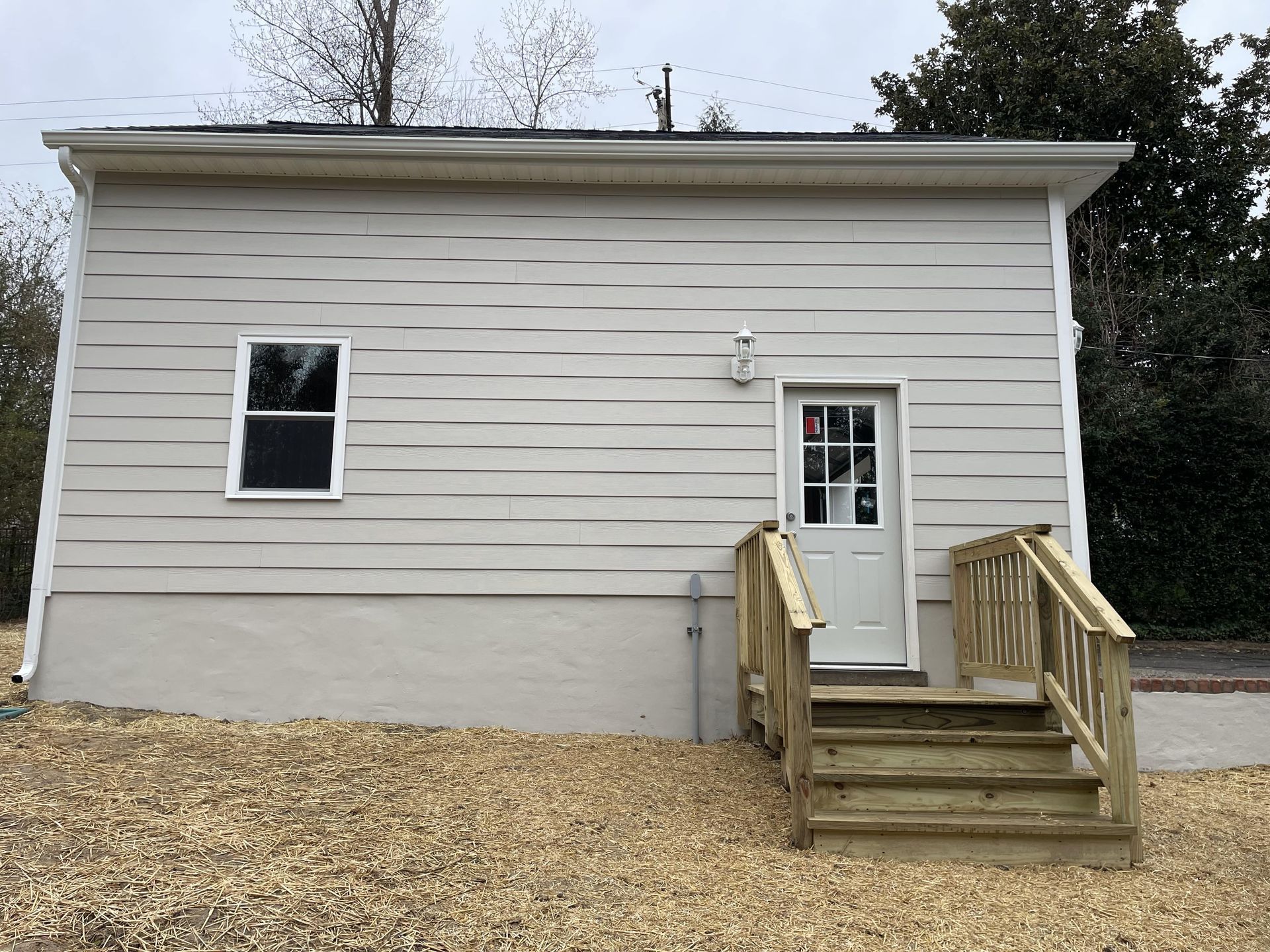 A small white house with a wooden deck and stairs leading to the door.