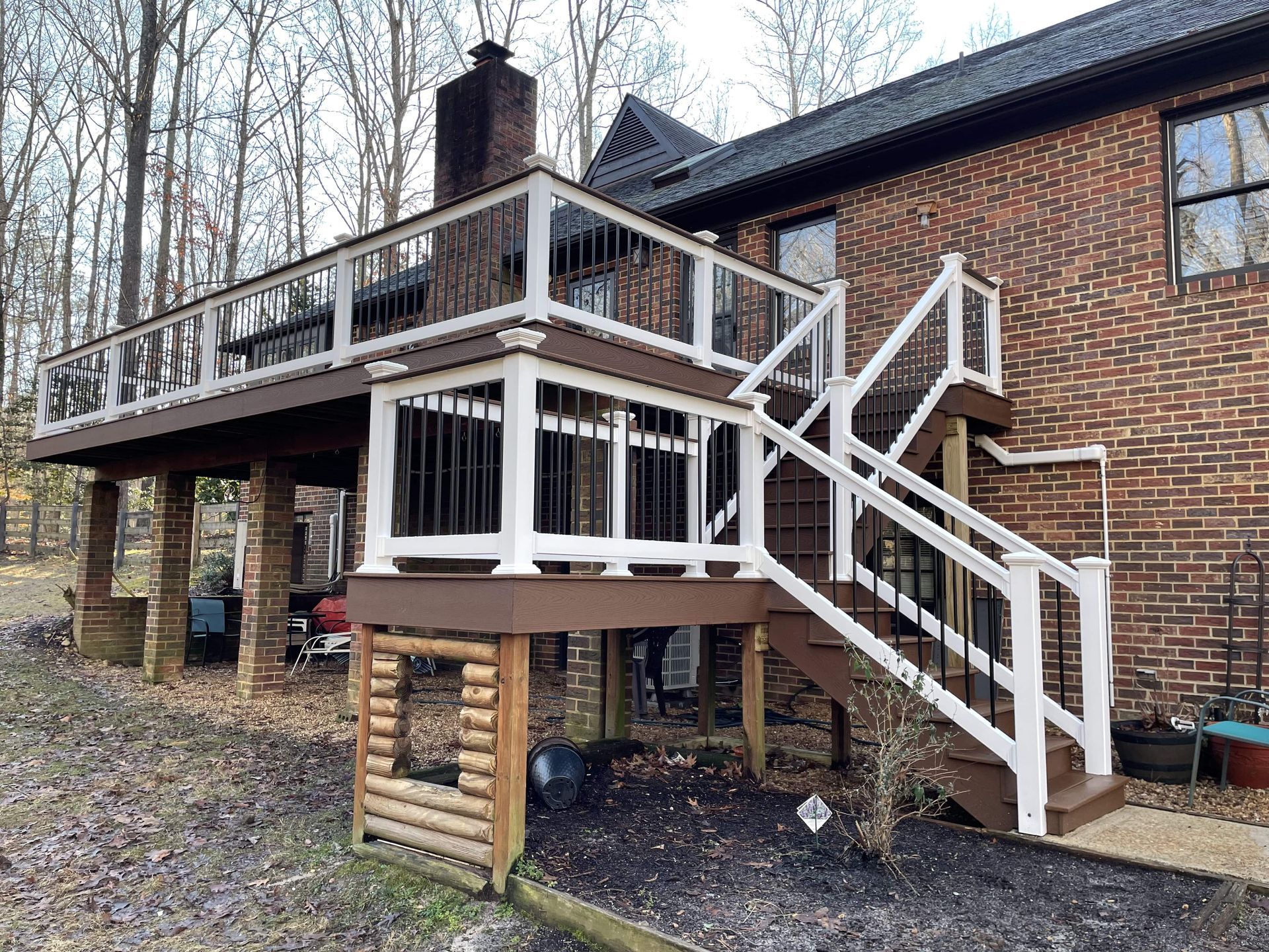 A deck with stairs leading up to it and a brick house in the background.