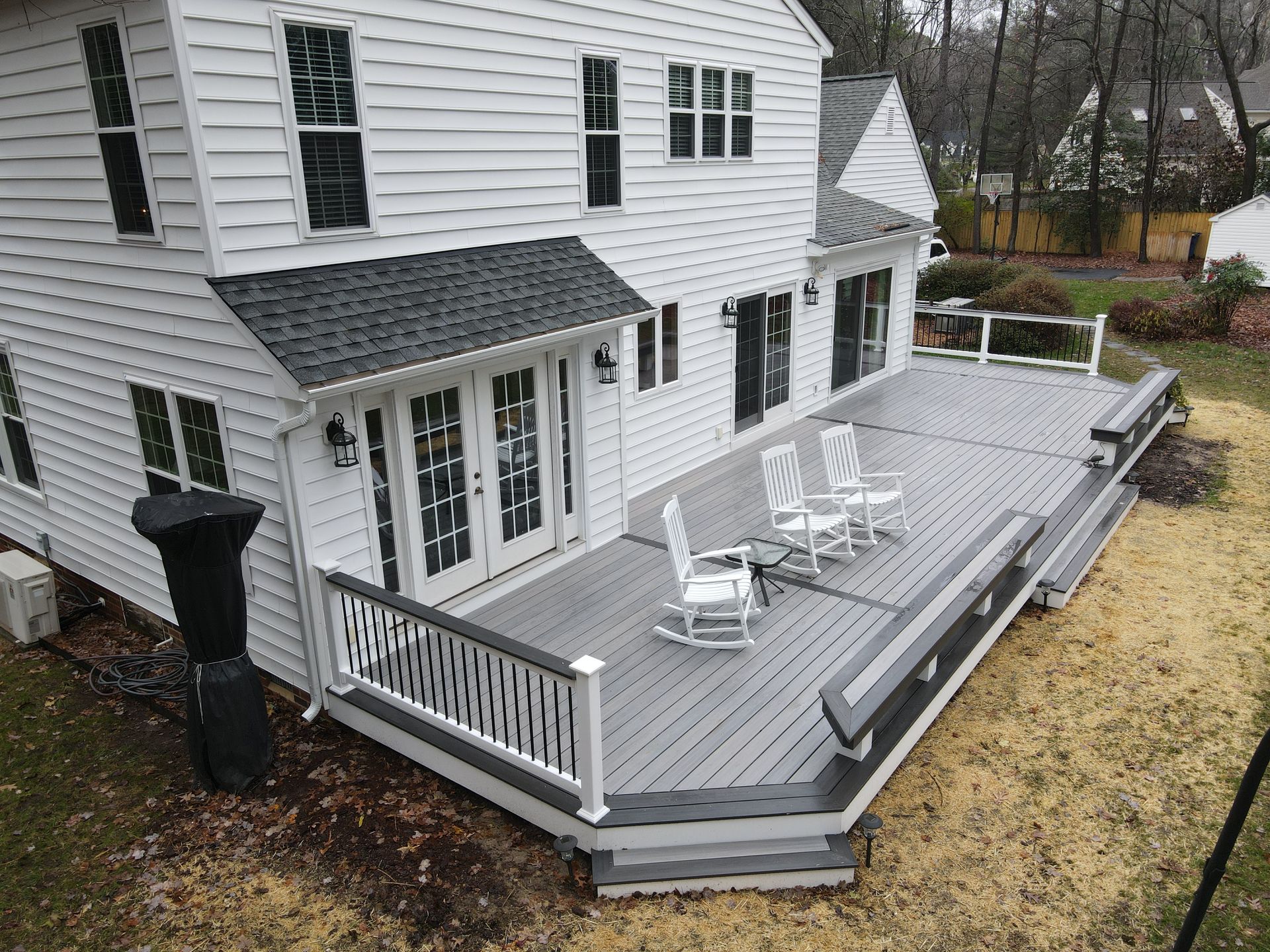 A large white house with a large deck with rocking chairs on it.