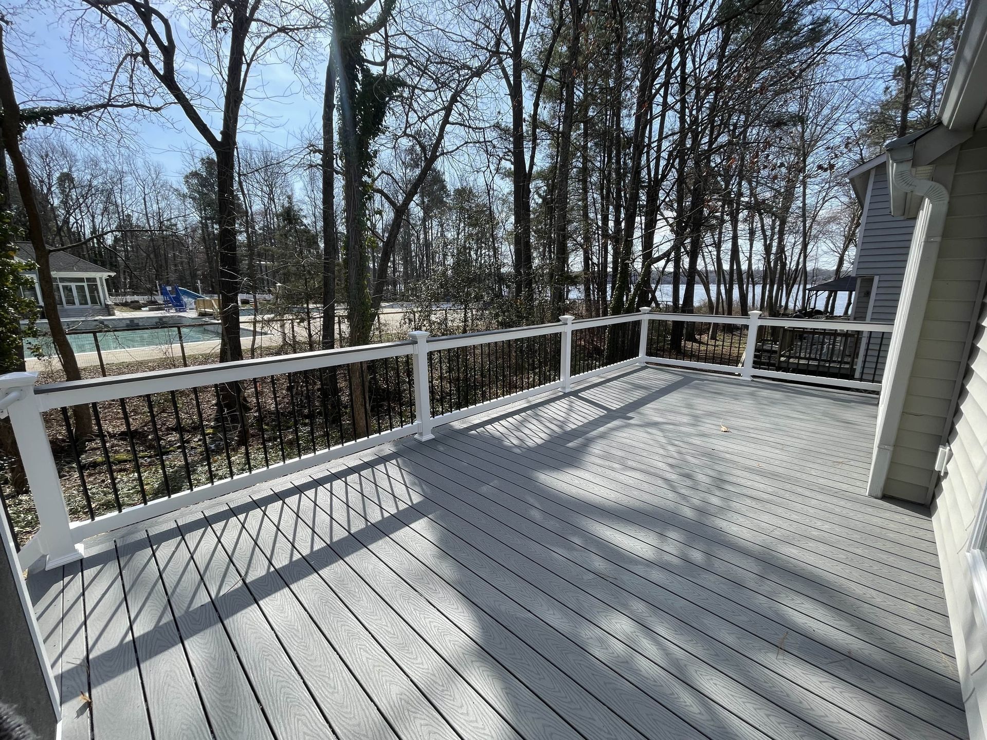 A large gray deck with a white railing and trees in the background.