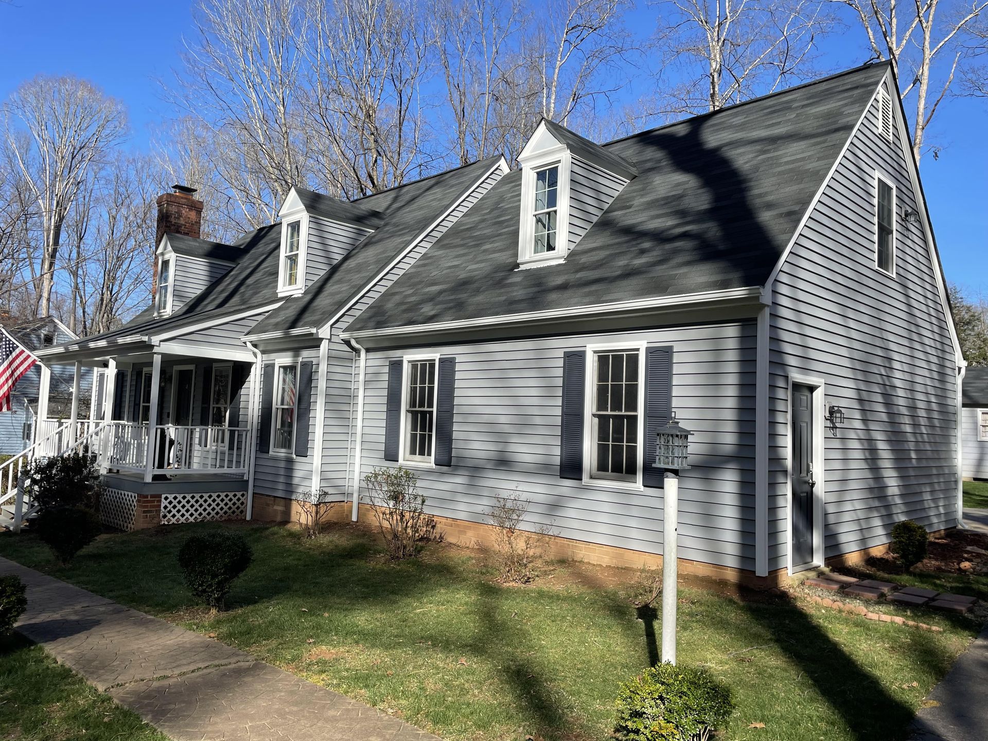 A white house with a black roof and a porch on a sunny day.