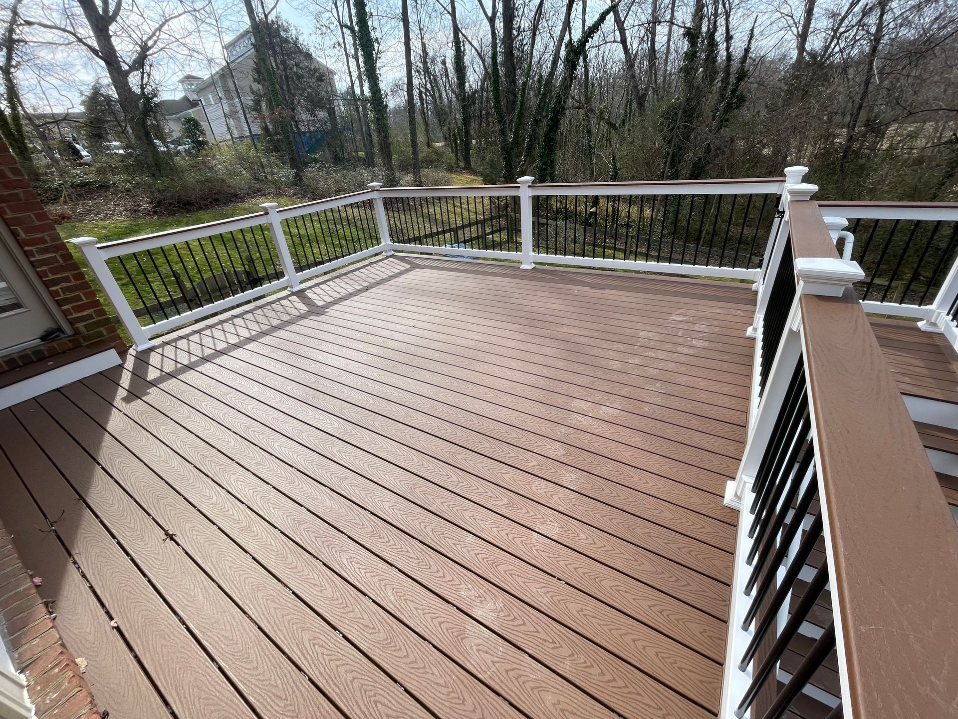 A large wooden deck with a white railing and trees in the background.