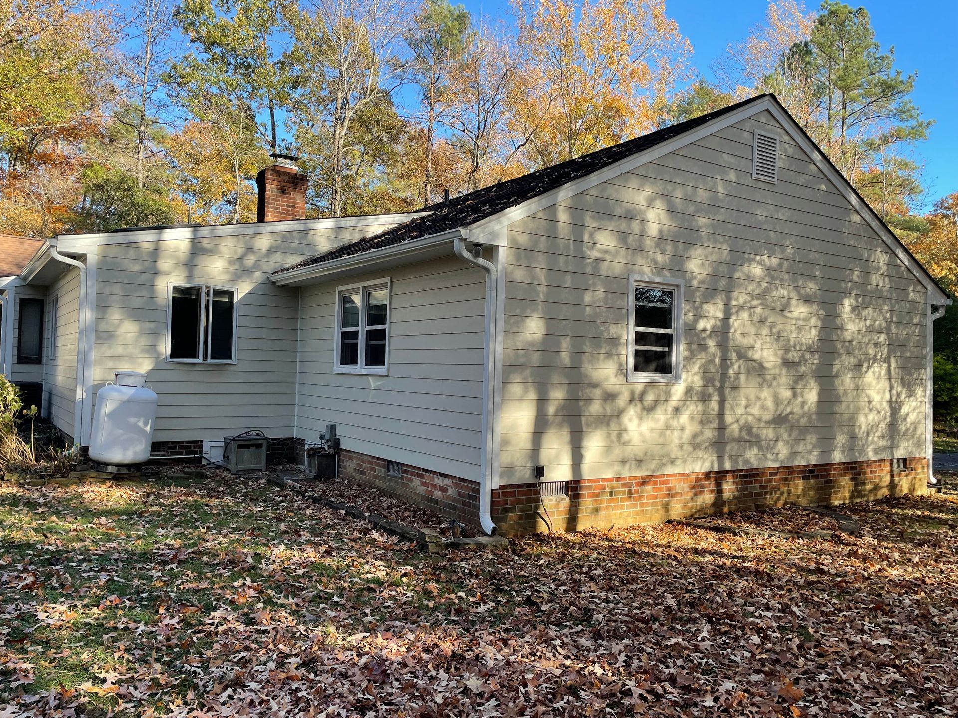 The back of a house with a lot of leaves on the ground.