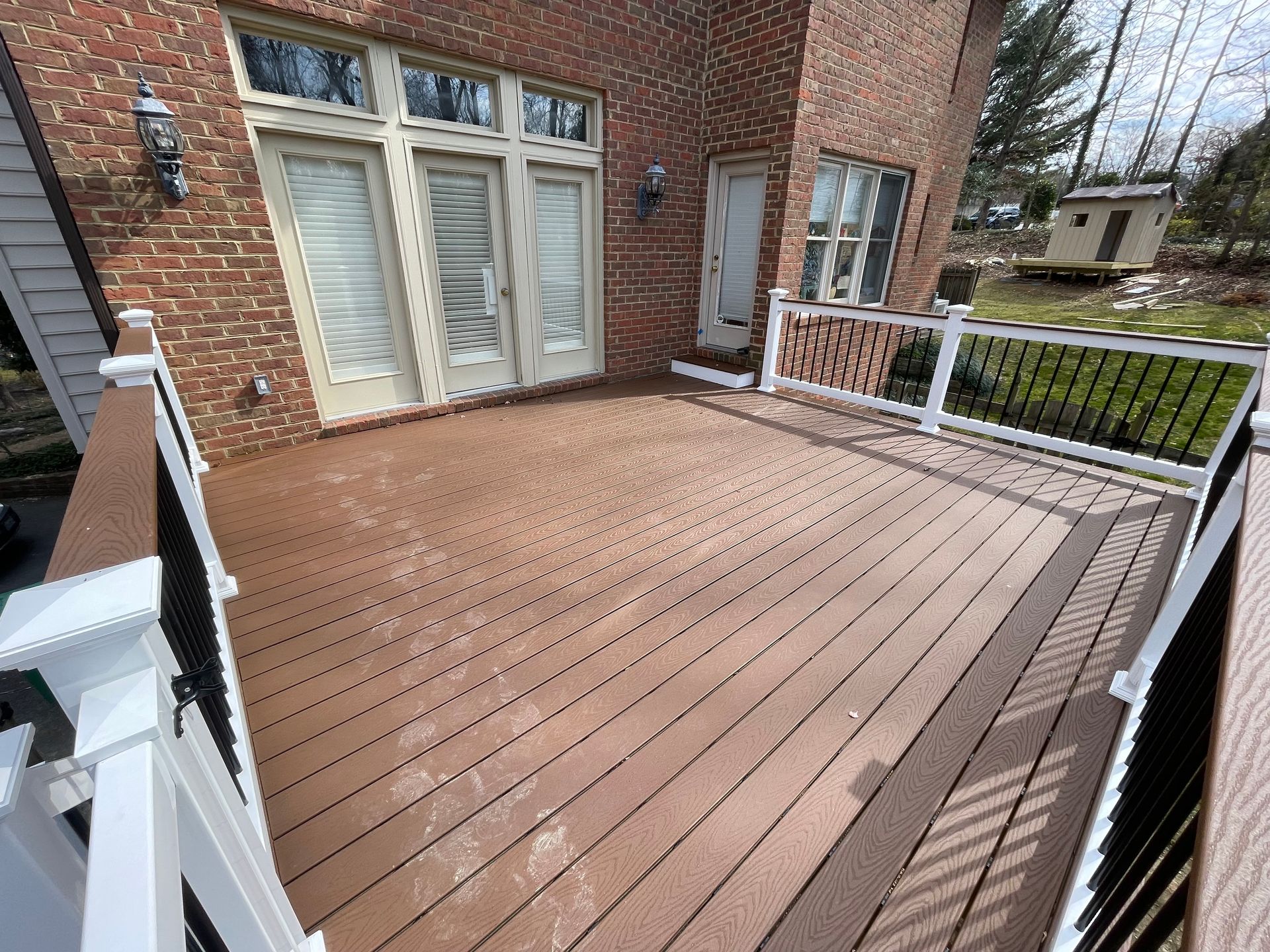 A wooden deck with a white railing in front of a brick house.