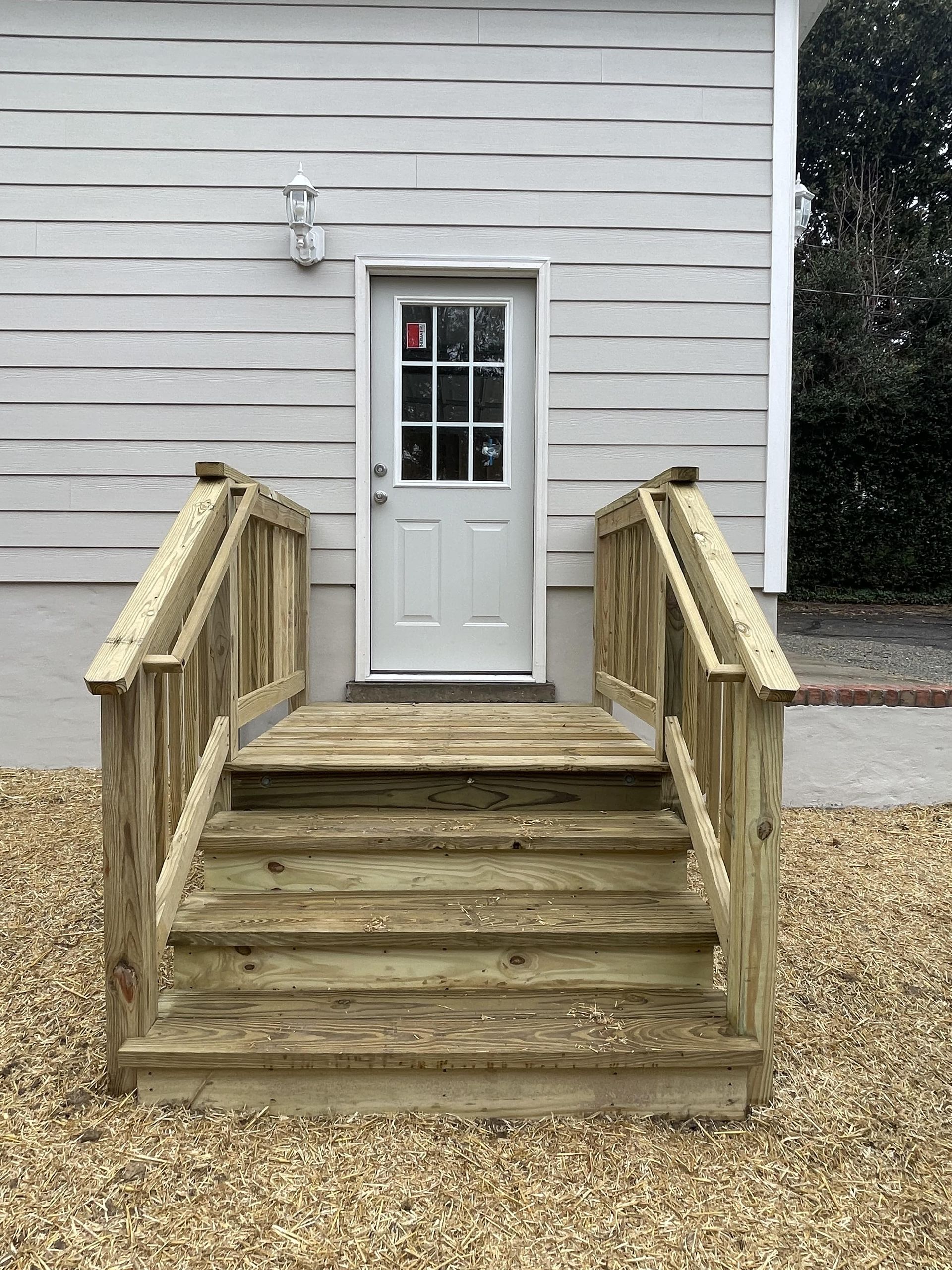 A white house with a wooden deck and stairs leading to the door.