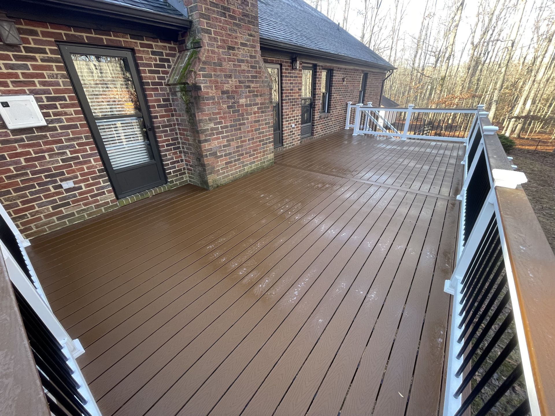 A large wooden deck with a white railing is in front of a brick house.