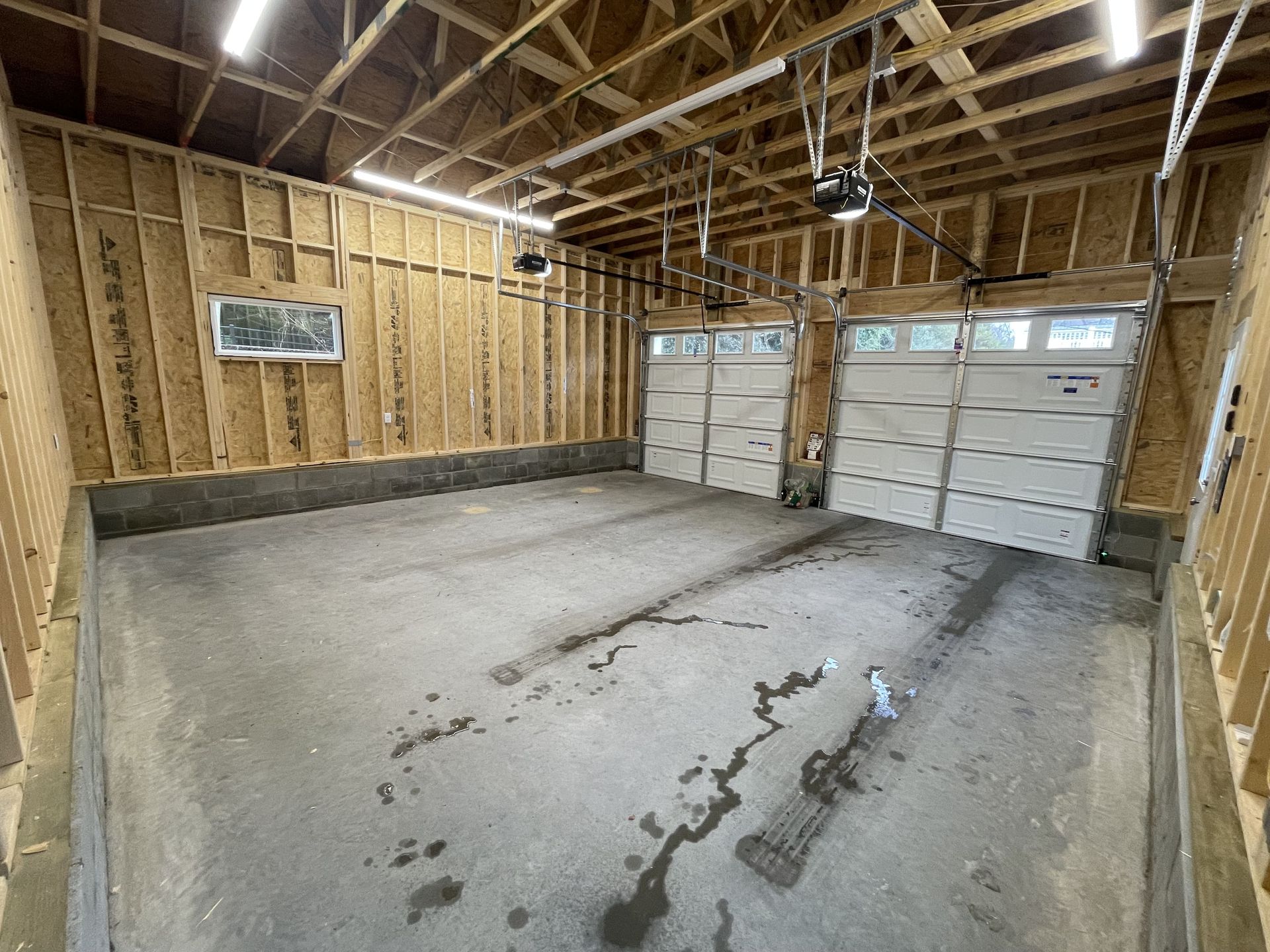 An empty garage with two garage doors and a concrete floor.