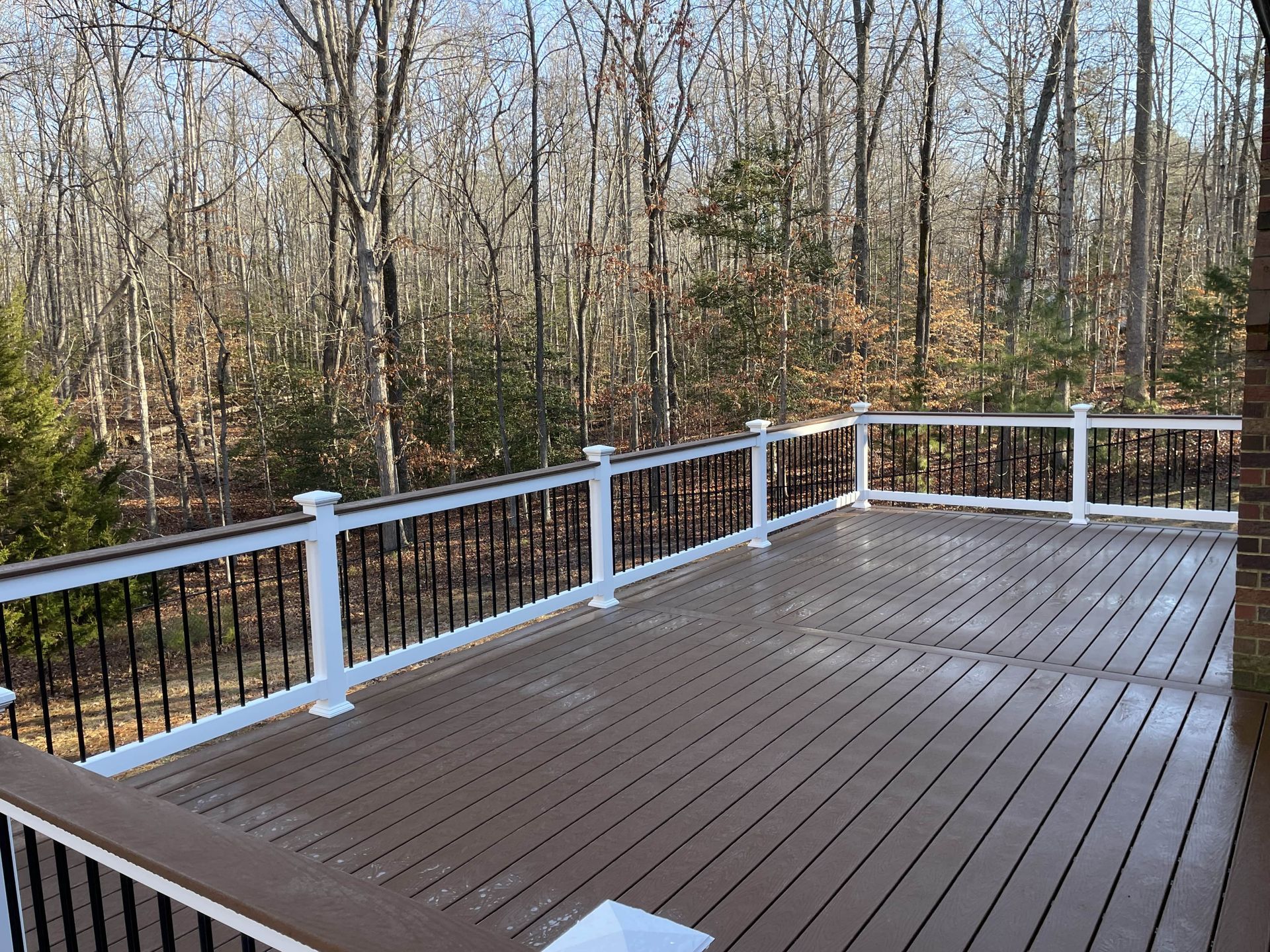 A large wooden deck with a white railing and trees in the background.