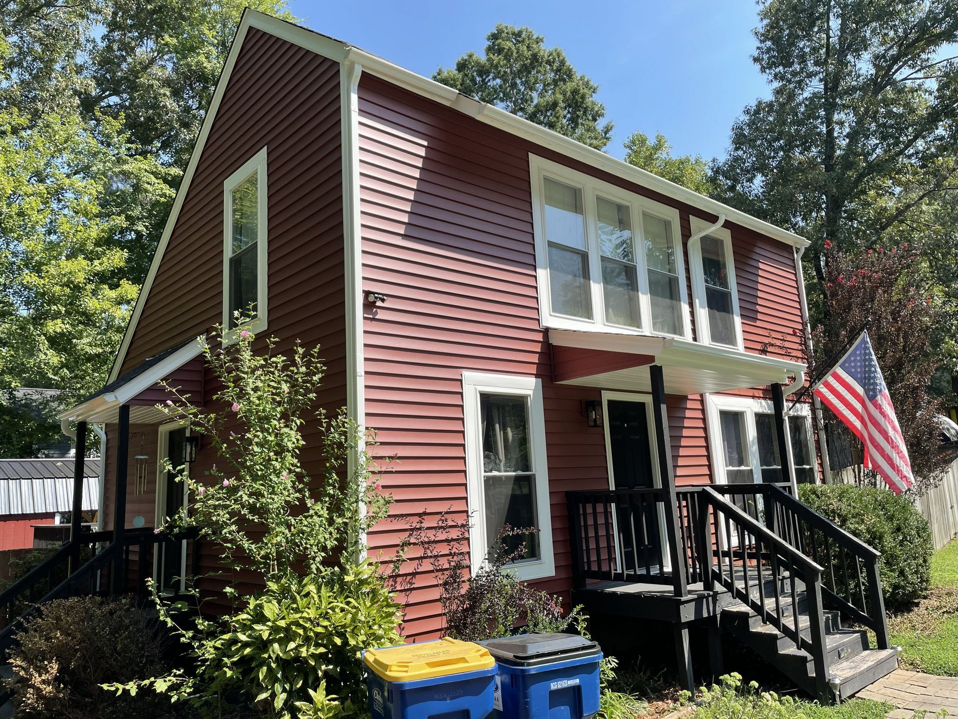 Red two-story house with black porch railings and an American flag.