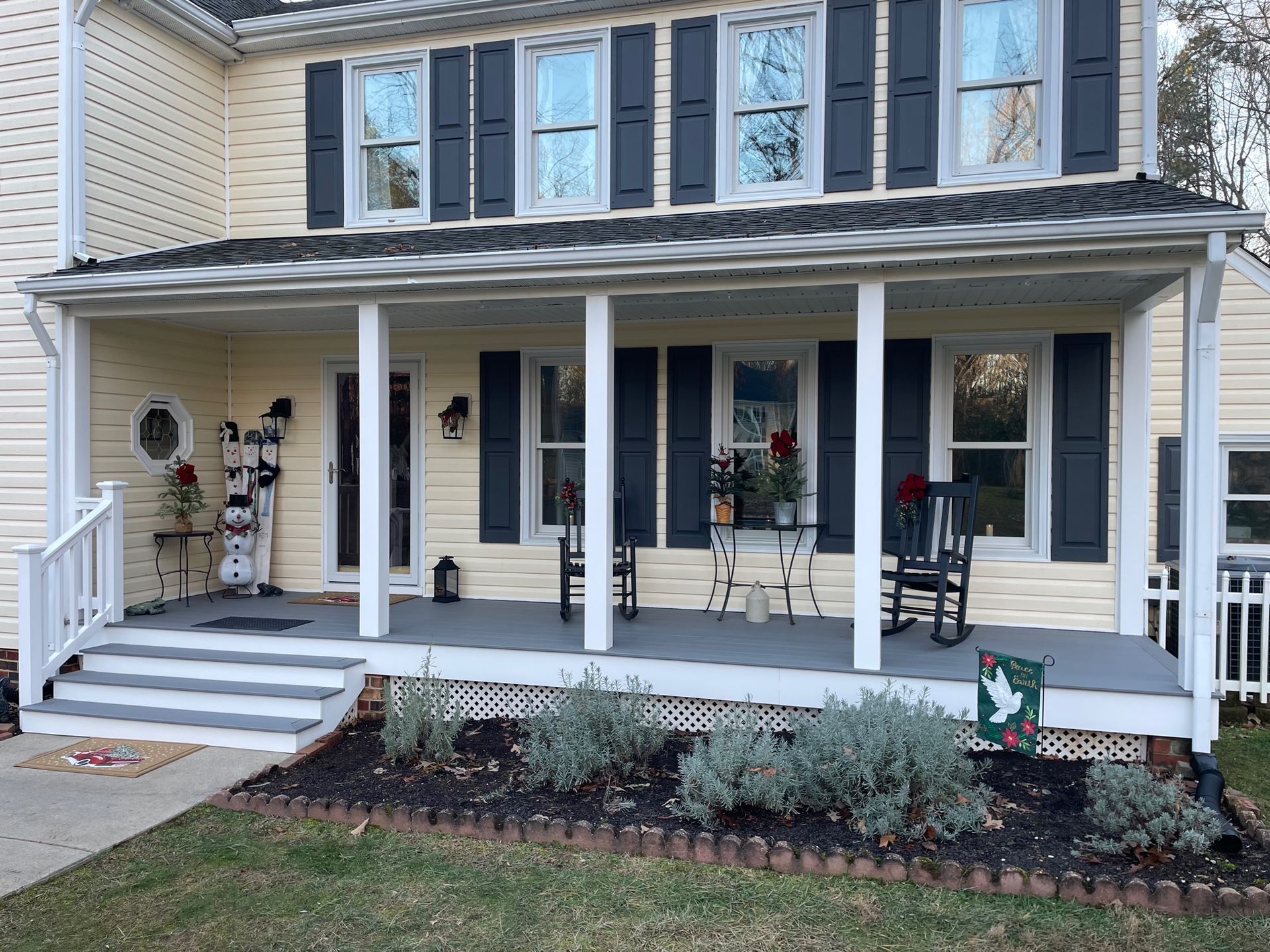 A yellow house with black shutters and a porch with rocking chairs.