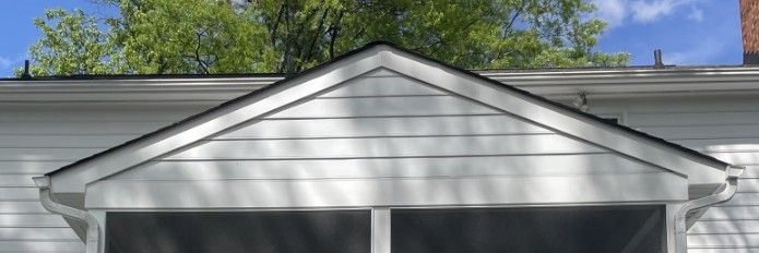 A white house with a screened in porch and a roof.
