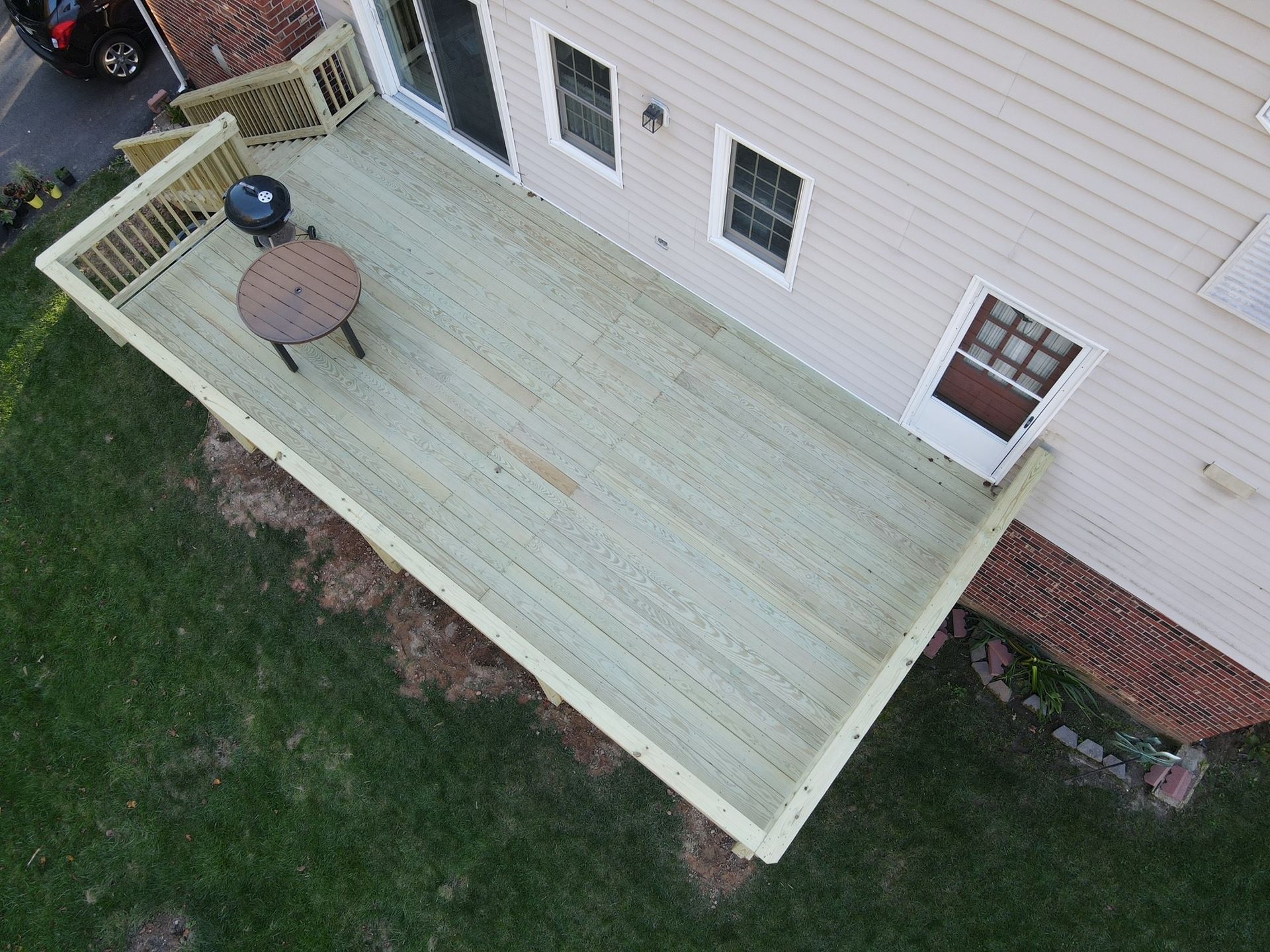 An aerial view of a wooden deck with a table and grill.