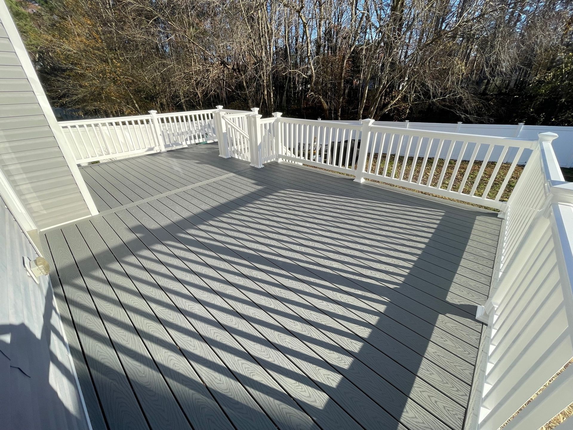 A gray deck with a white railing and trees in the background.