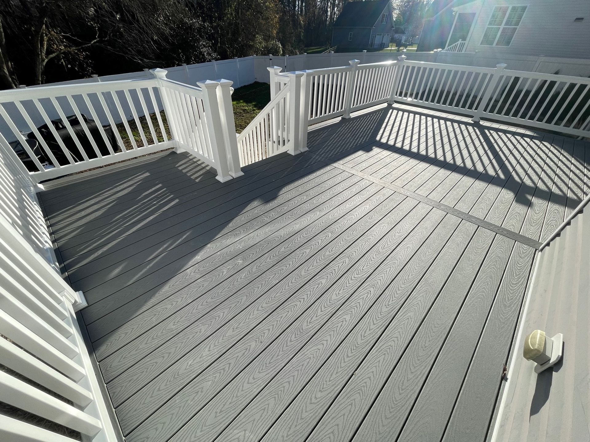 A large gray deck with a white railing and a white fence.