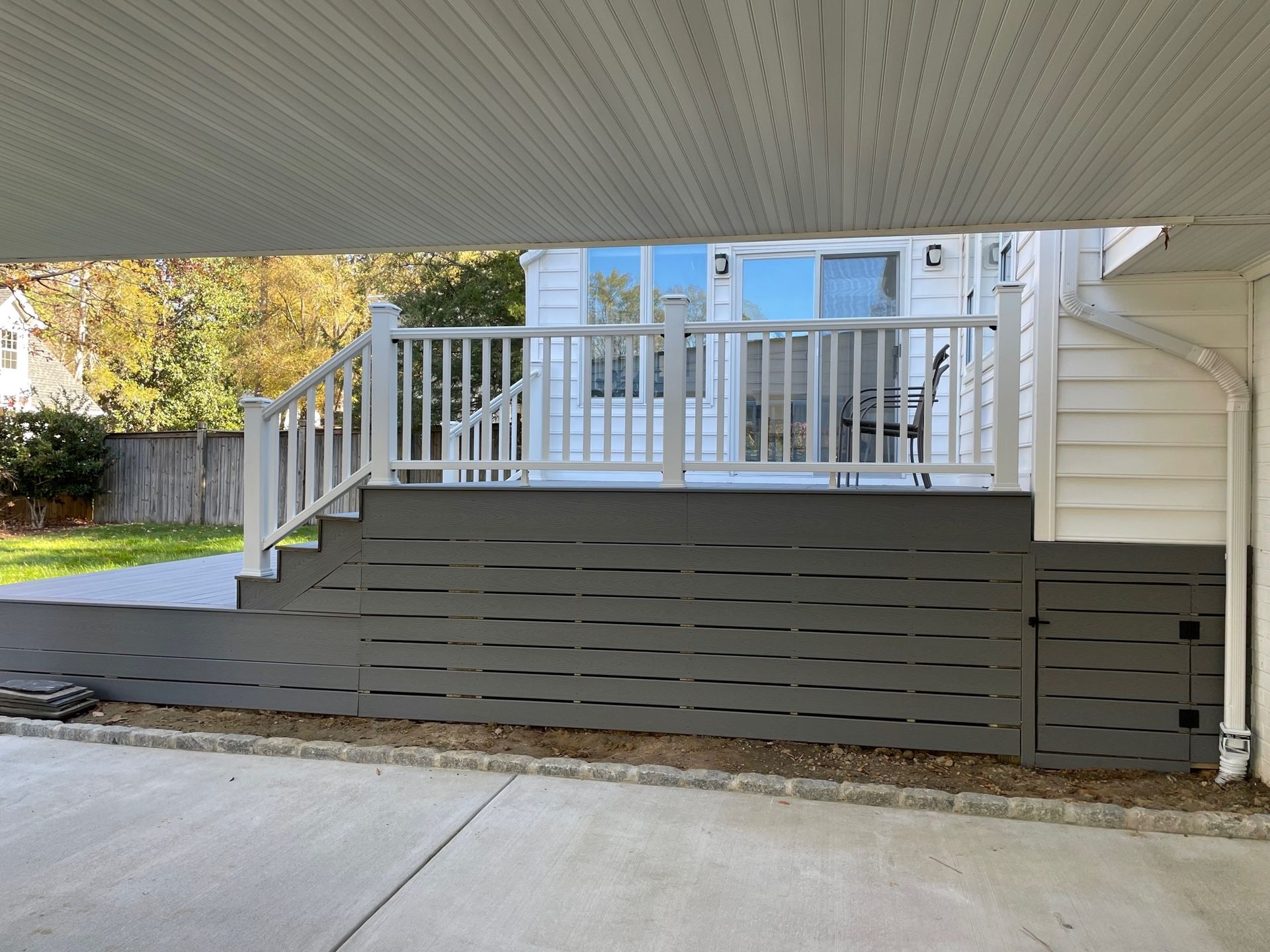 A white house with a deck and stairs under a carport.