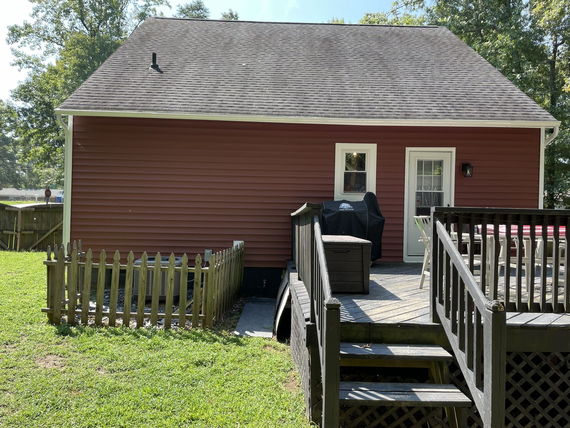 Red-sided house with dark roof, deck, and small fence on green lawn.