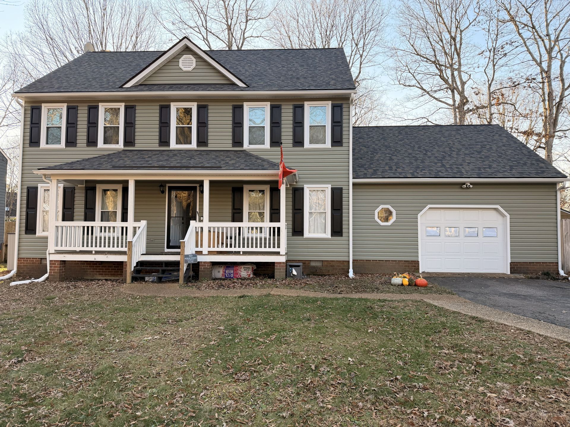 Two-story house with a white porch and attached garage, gray siding, black shutters, and autumn pumpkins.