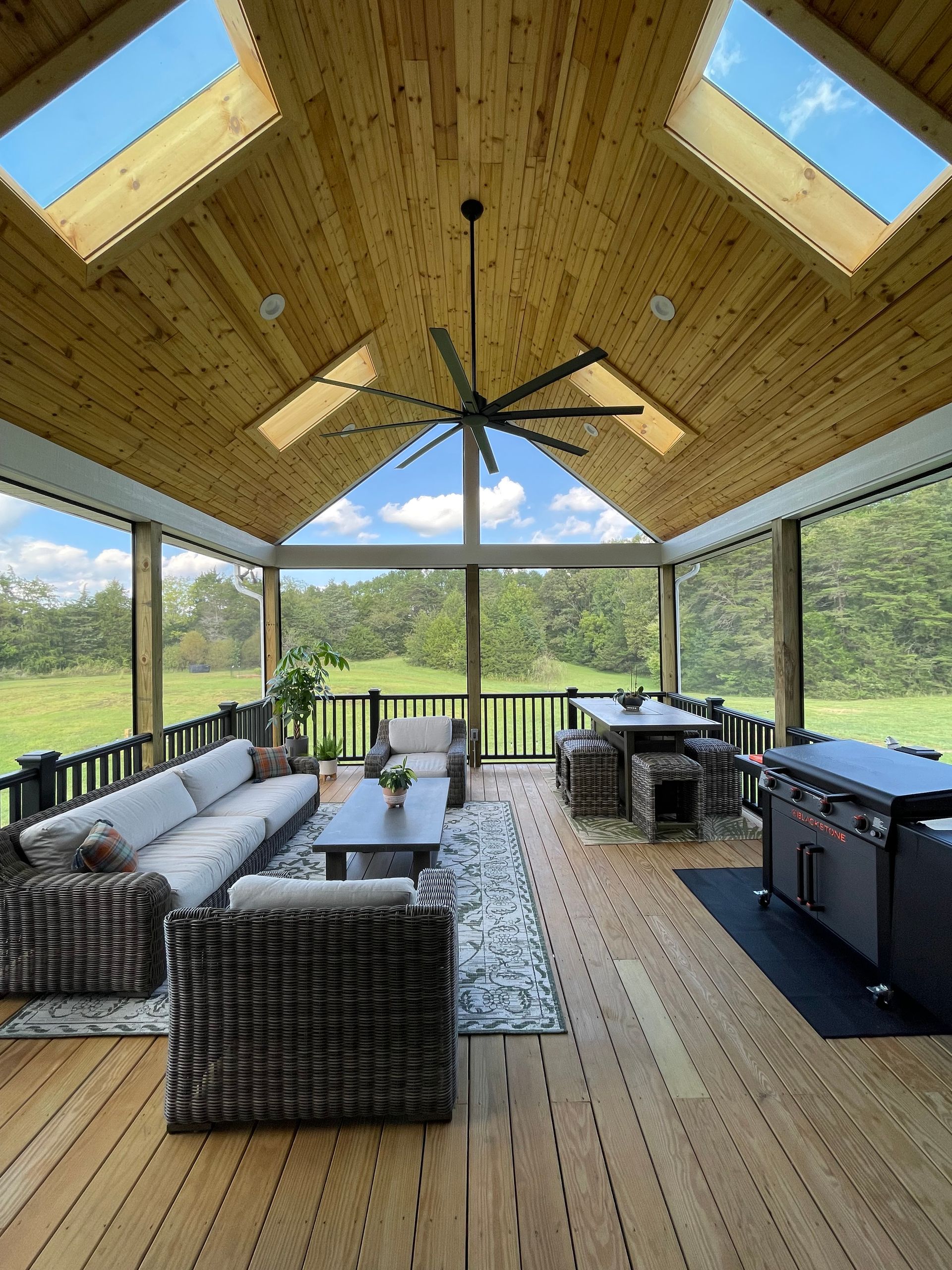 A screened in porch with a lot of furniture and a ceiling fan.