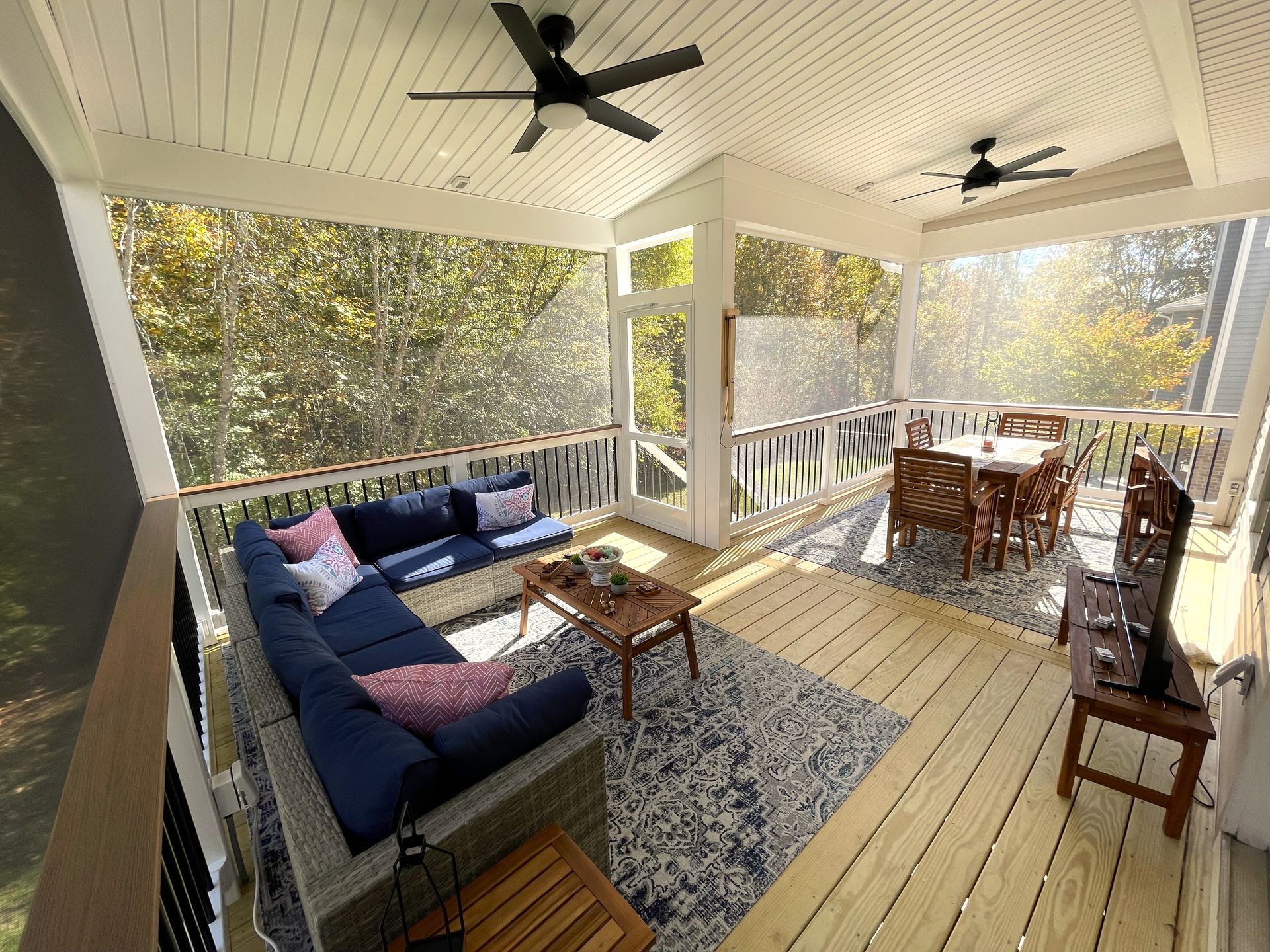 A screened in porch with a couch , table , and television.