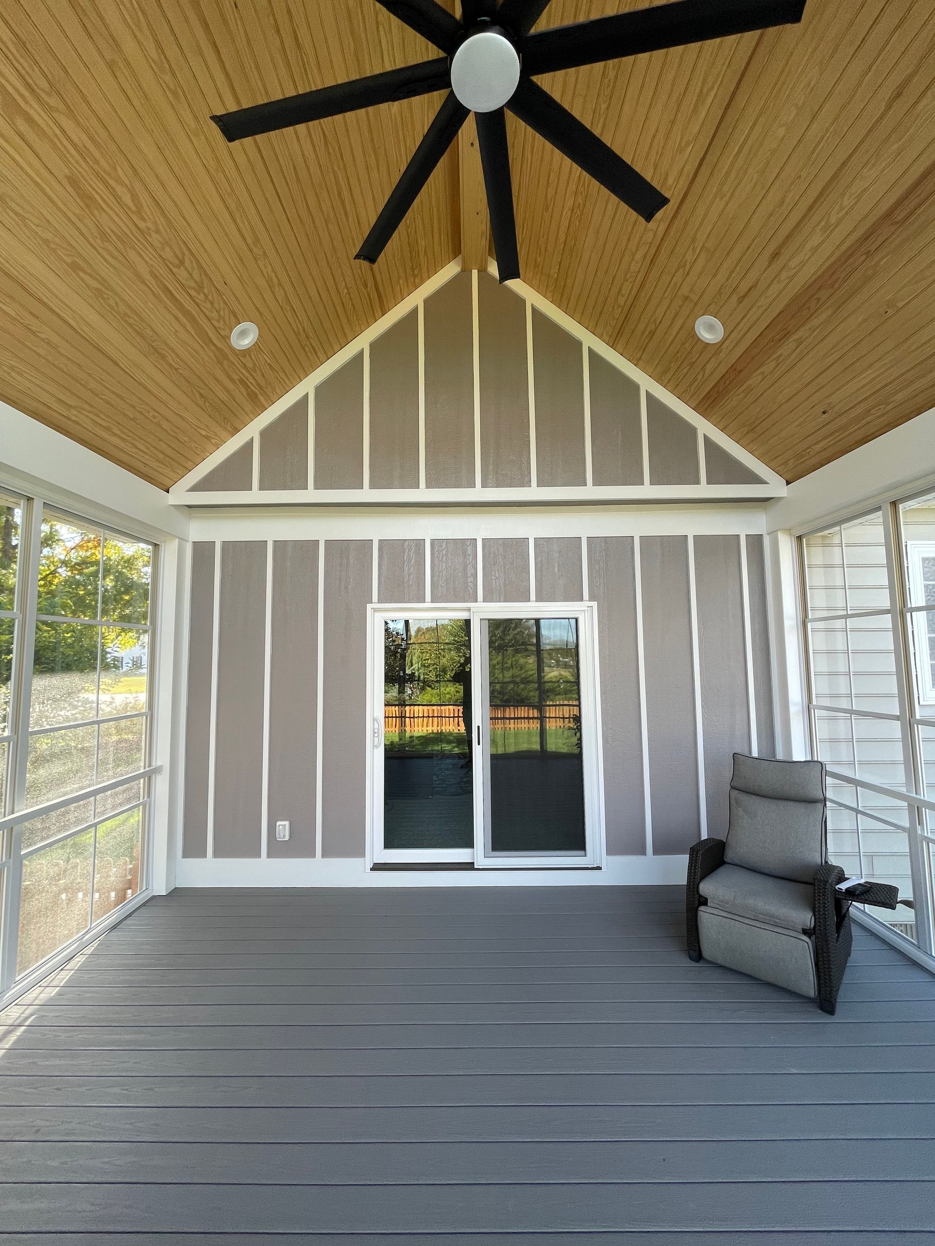 A screened in porch with a chair and ceiling fan