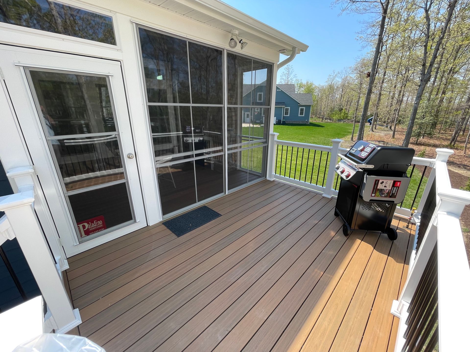 A screened porch with a composite deck, grill, and white railing on a sunny day.