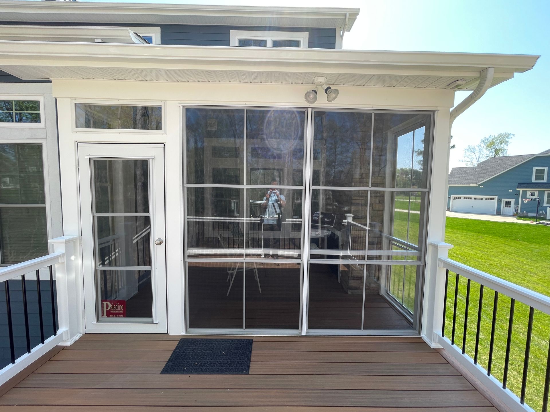 Screened porch with brown deck, white trim, and a blue house in the background.