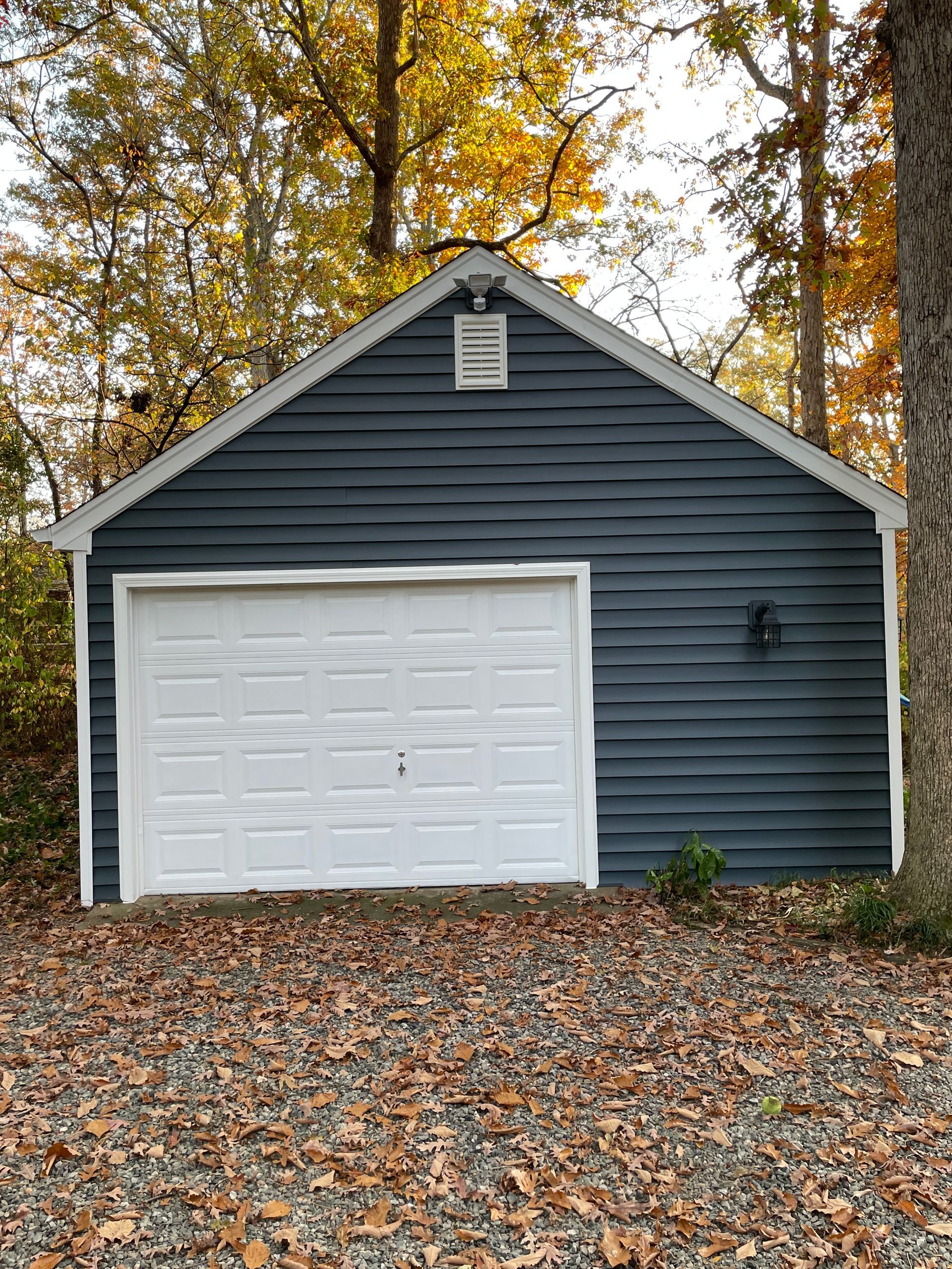Blue-sided garage with white garage door, surrounded by fall foliage.