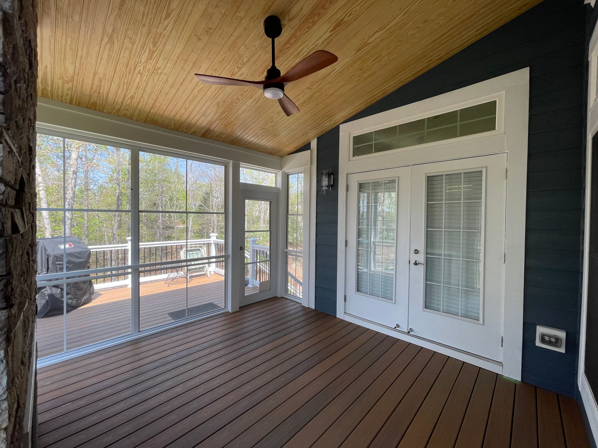 Screened porch with wooden deck, ceiling fan, and doors leading to a deck and interior.