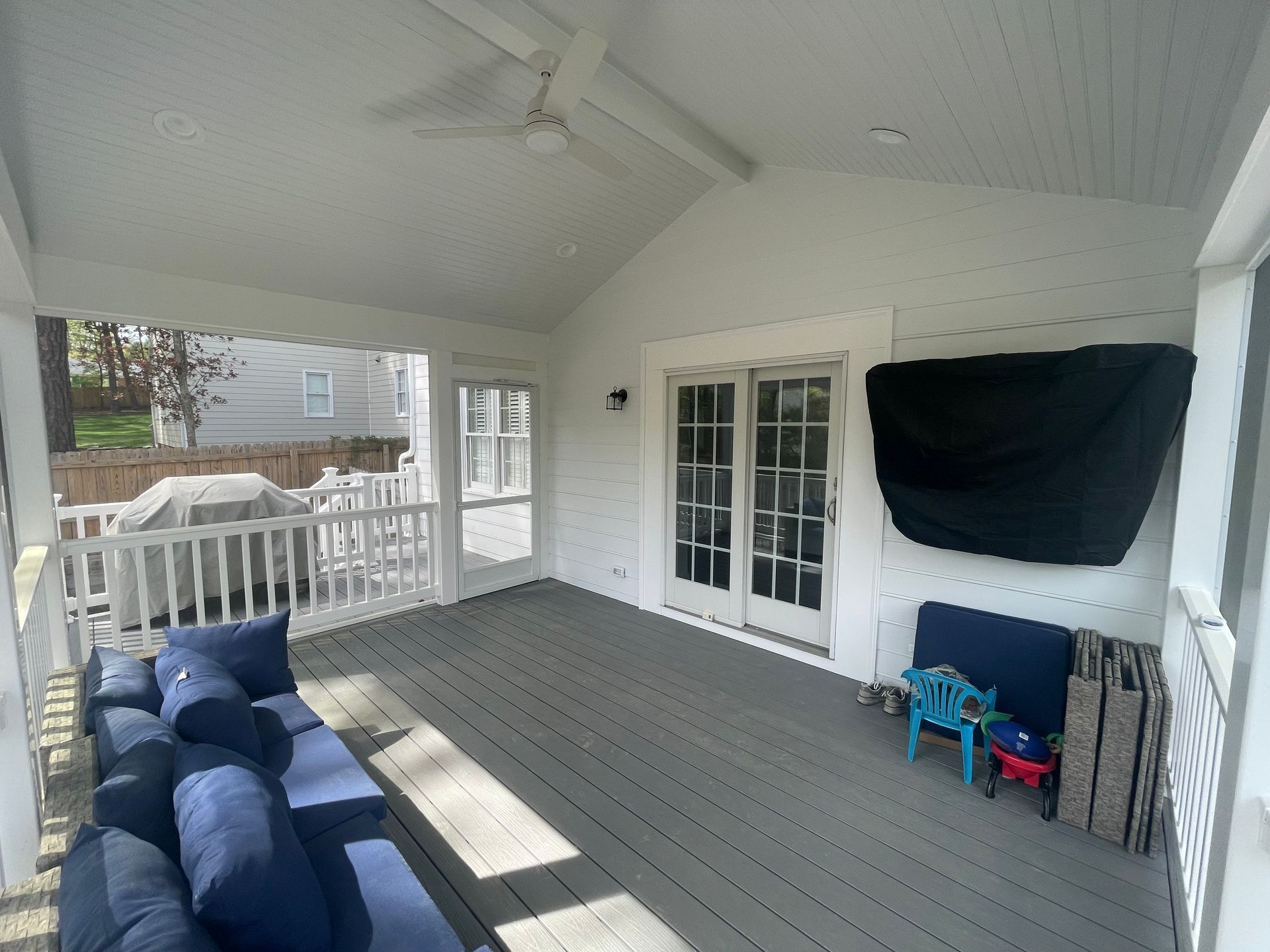Covered porch with blue couch, gray floor, white railing, and a TV with cover.