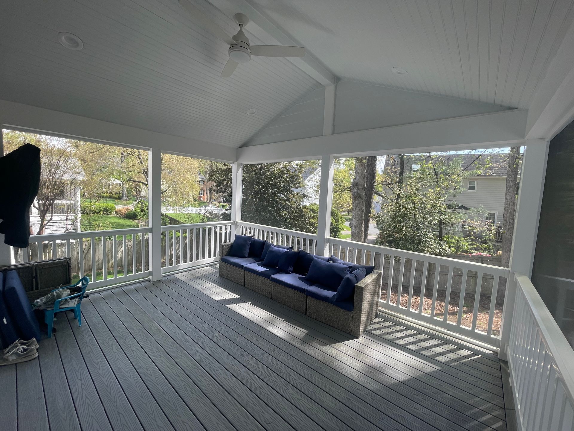 Covered porch with gray flooring, white railings, and a blue sofa. Trees and greenery are visible outside.