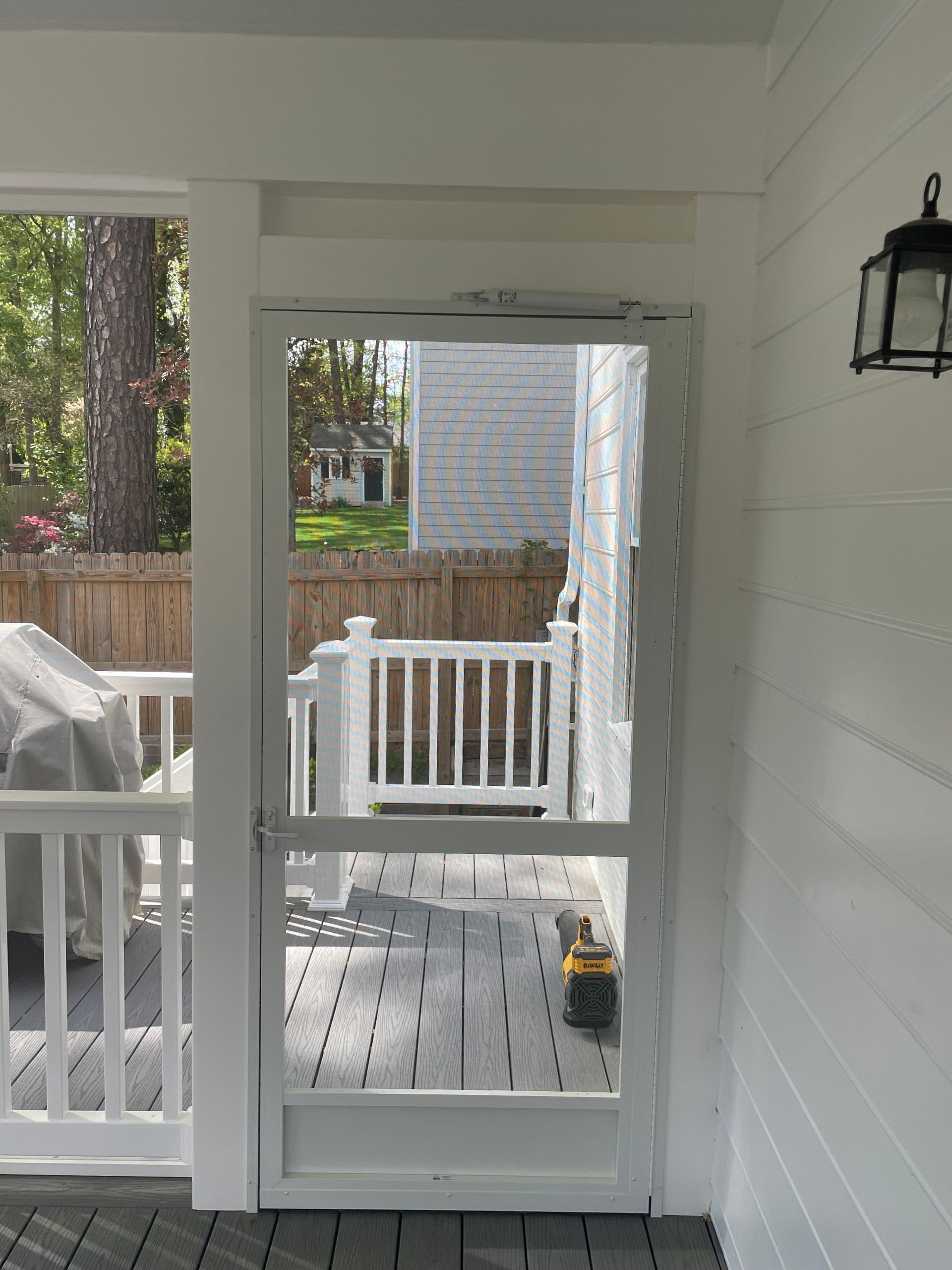 White screened porch door, leading to a wooden deck with a grill and white railing.